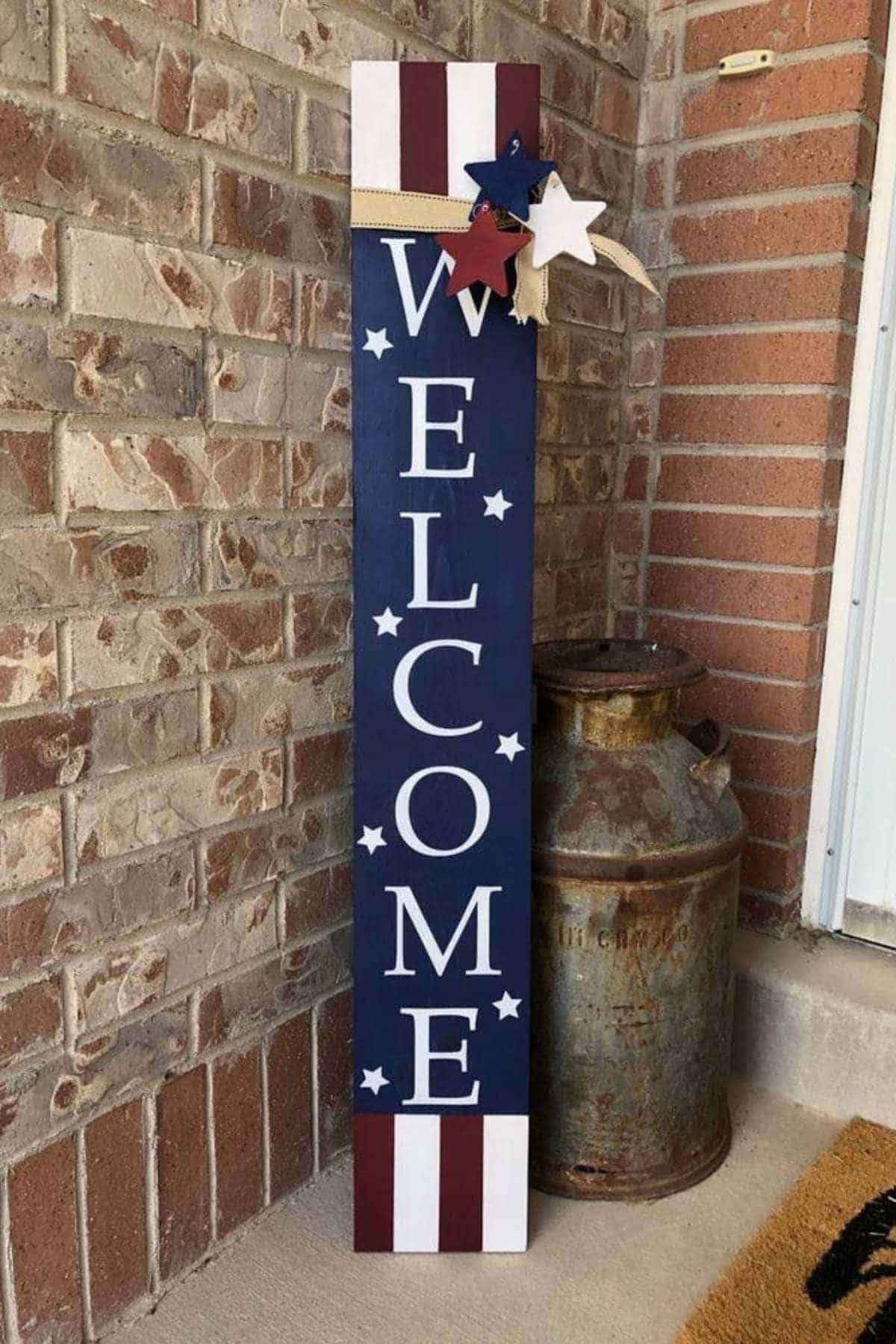 A vertical "WELCOME" sign with patriotic stars and stripes, next to a rusty milk can.