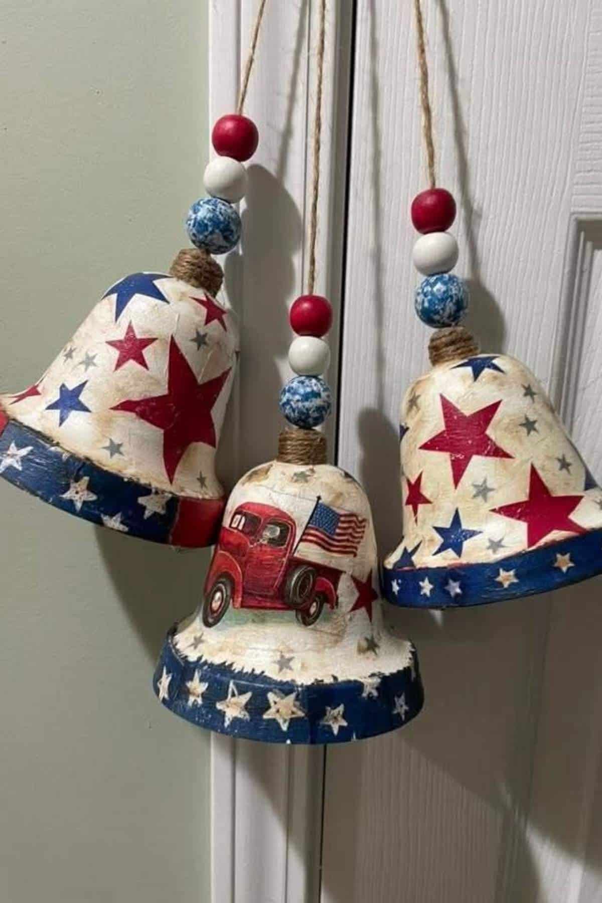 Three decorative bells with red, white, and blue stars, two with only stars and one with a red truck carrying an American flag, hanging by twine with beaded accents.