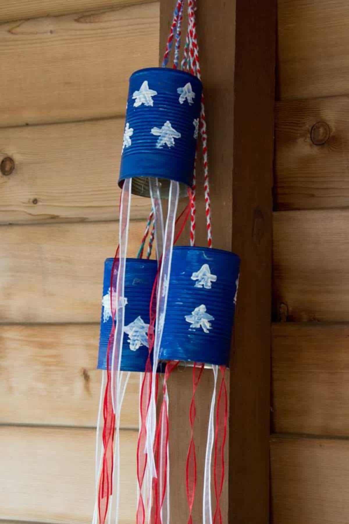Blue tin cans painted with white stars, decorated with red and white streamers, hang from a wooden structure.