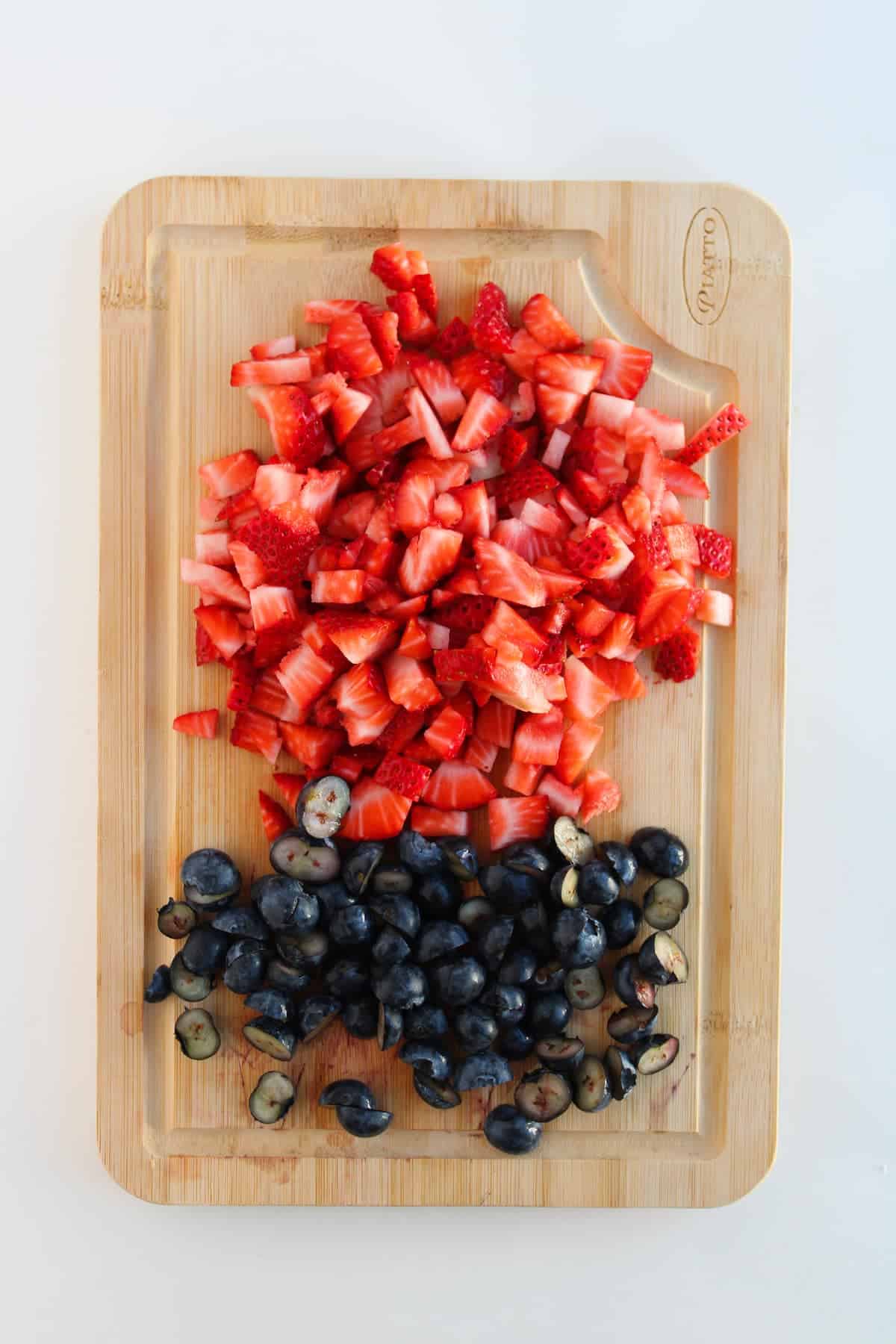 Chopped strawberries and halved blueberries arranged on a wooden cutting board.