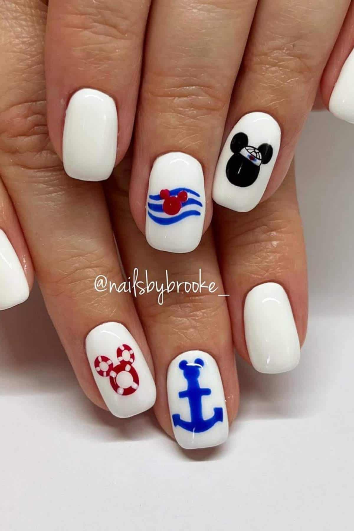 Hand with white nail polish; accent nails feature nautical and mouse-themed designs in red, blue, and black.