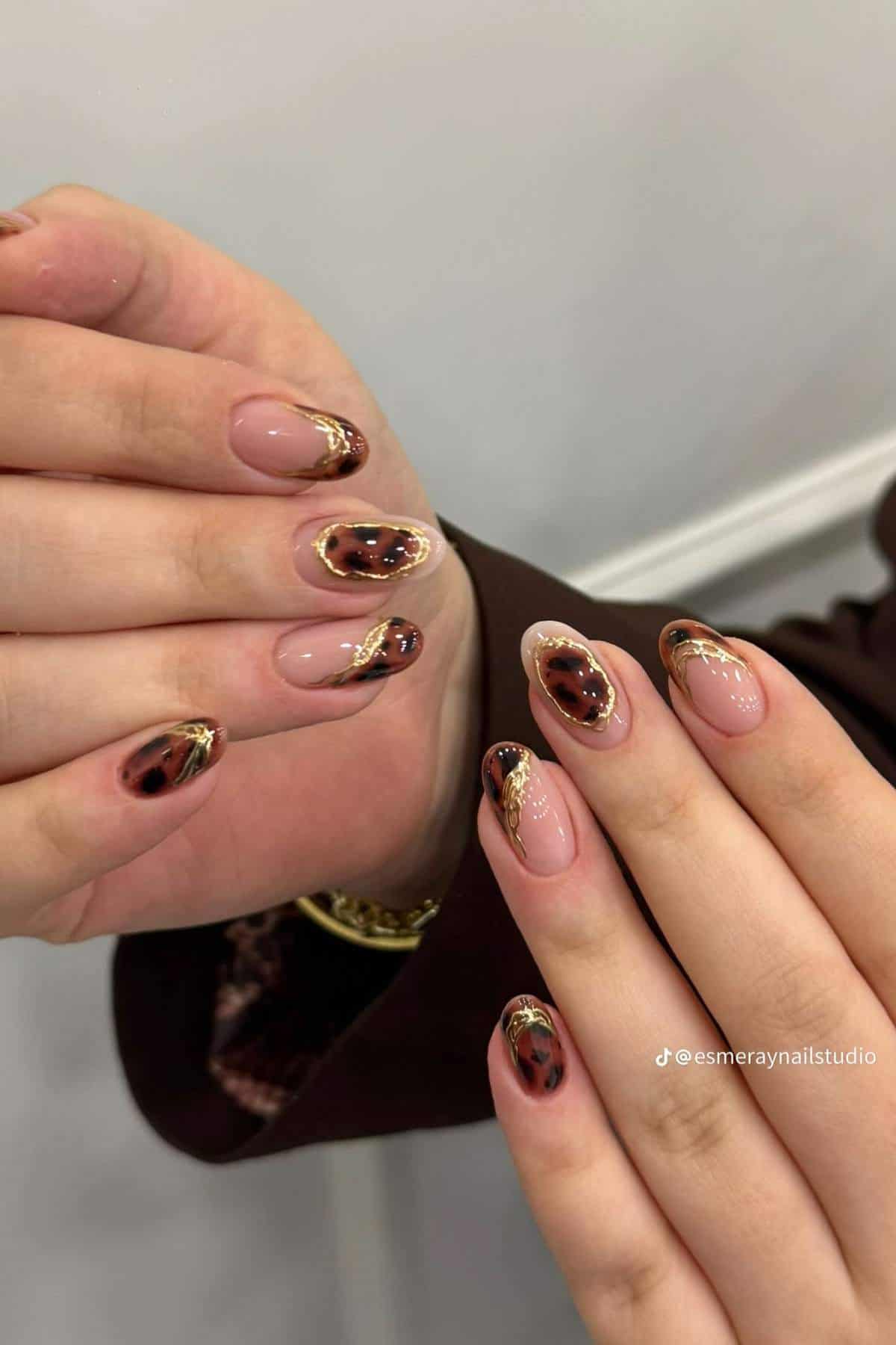 Close-up of hands with almond-shaped nails featuring a leopard design and gold accents on a neutral base.