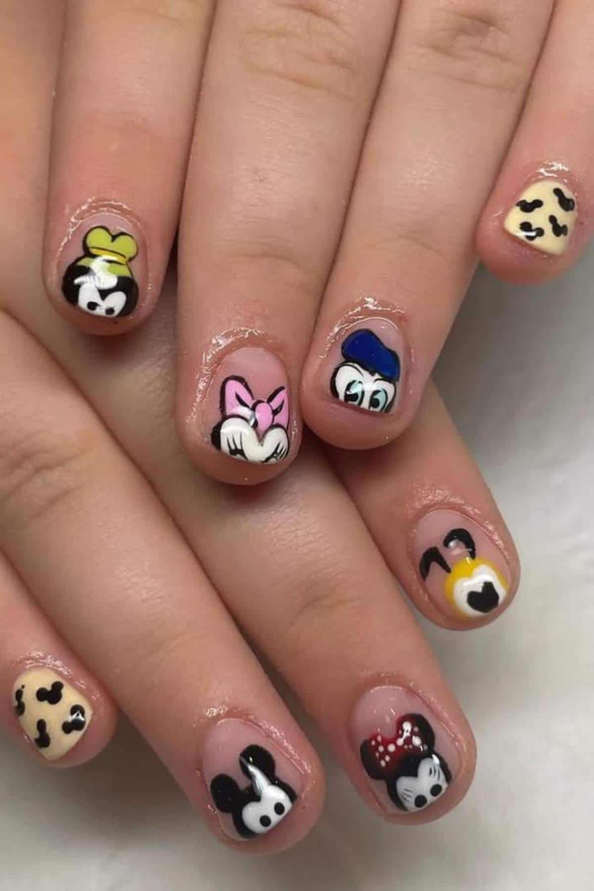 Short nails painted with Disney character nail art, featuring Mickey Mouse, Minnie Mouse, Donald Duck, Goofy, and Pluto on a nude base.