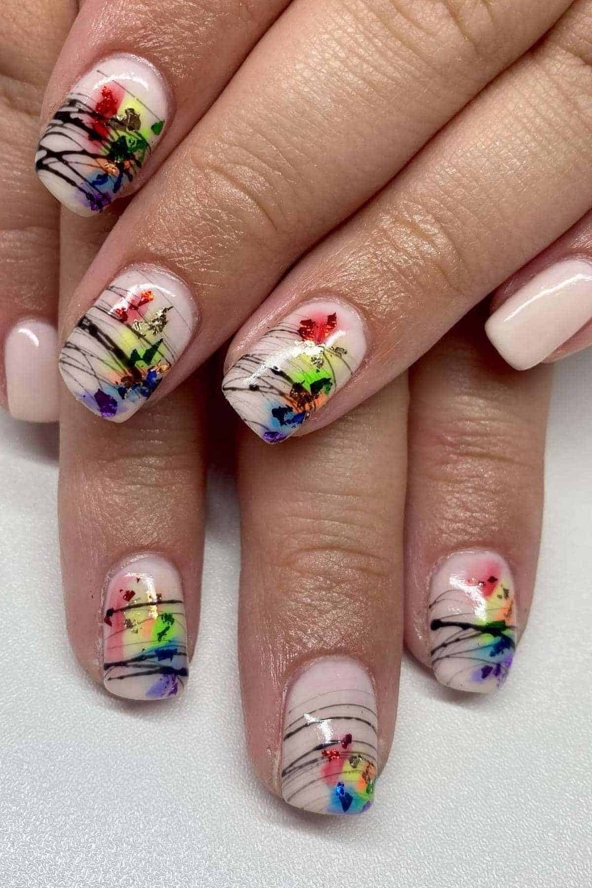 Close-up of manicured nails with a pale pink base, colorful abstract designs, and thin black lines on the tips.