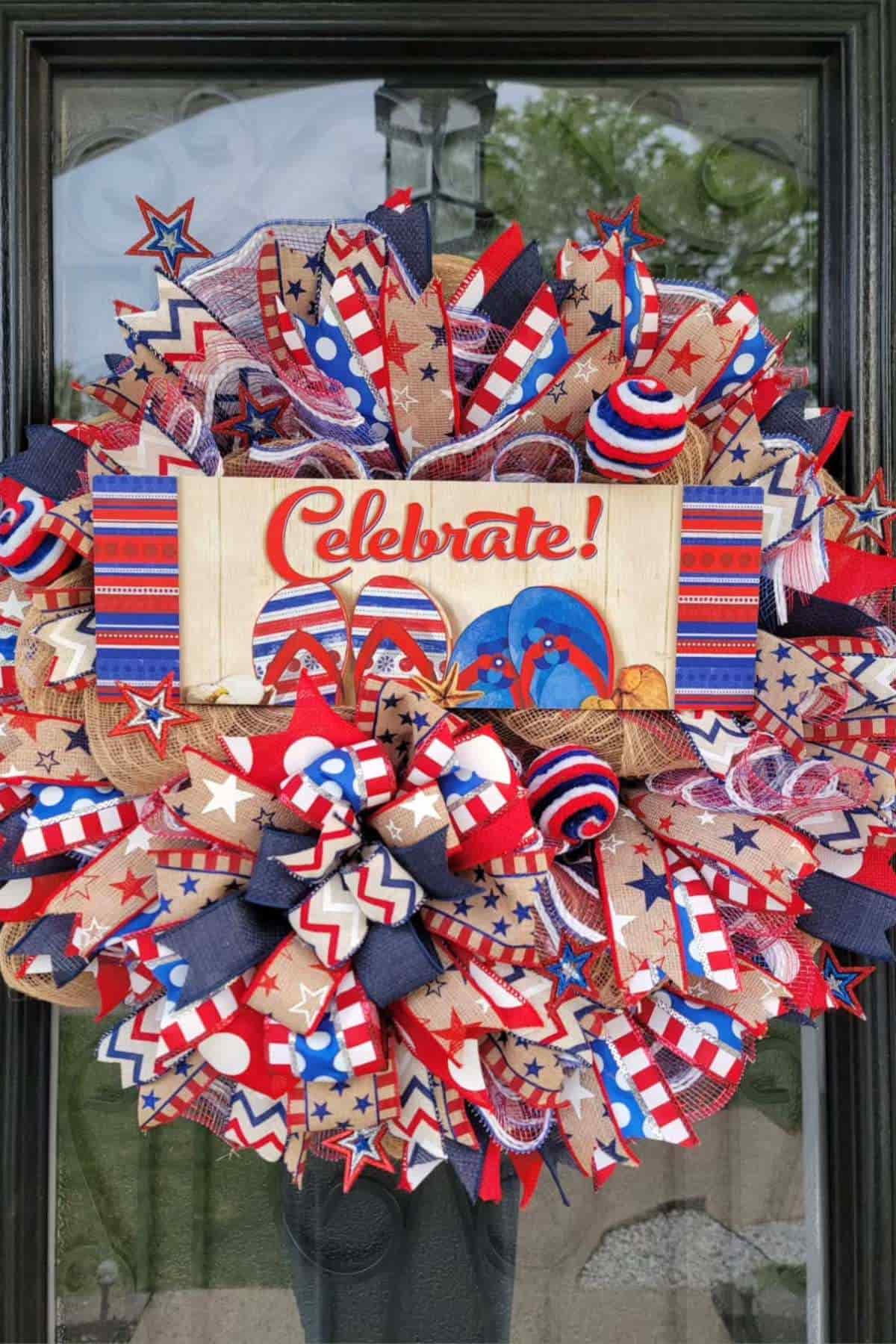 Patriotic wreath with red, white, and blue ribbons, stars, and a sign reading "Celebrate!" displayed on a door.