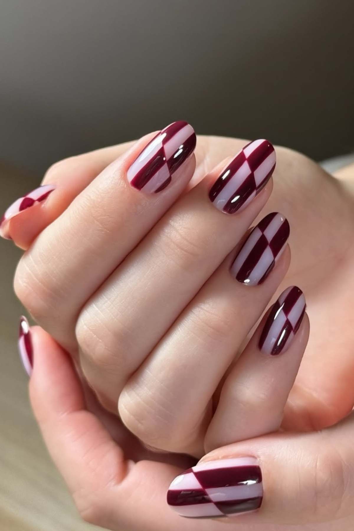 Close-up of hands with almond-shaped nails painted in burgundy and pale pink geometric stripe patterns.