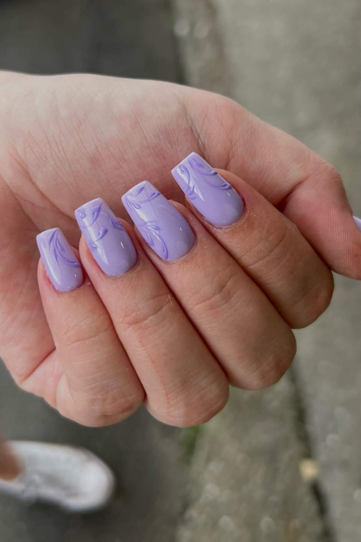 A hand with long, ballerina-shaped nails painted in glossy lavender polish with subtle marble-like patterns.