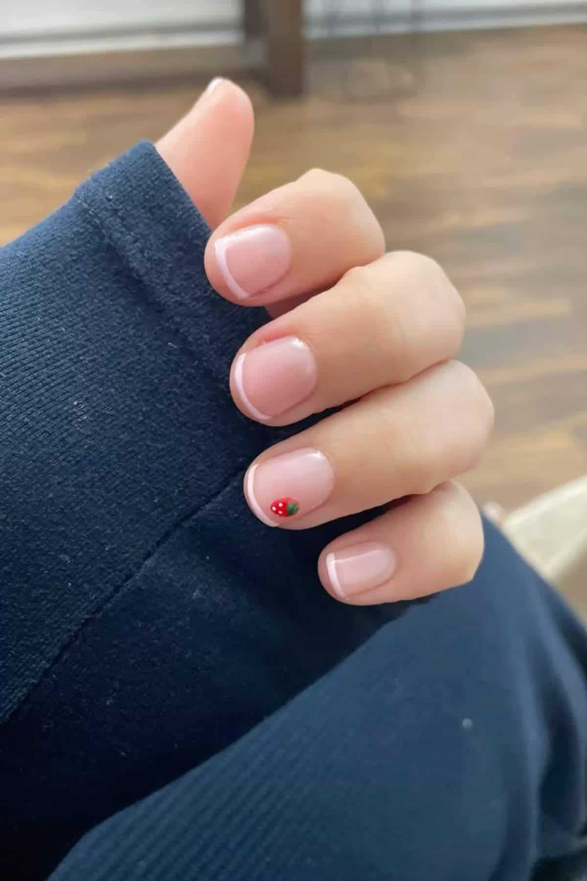 A hand with short, natural nails featuring a French manicure and a small red ladybug design on the ring finger nail.
