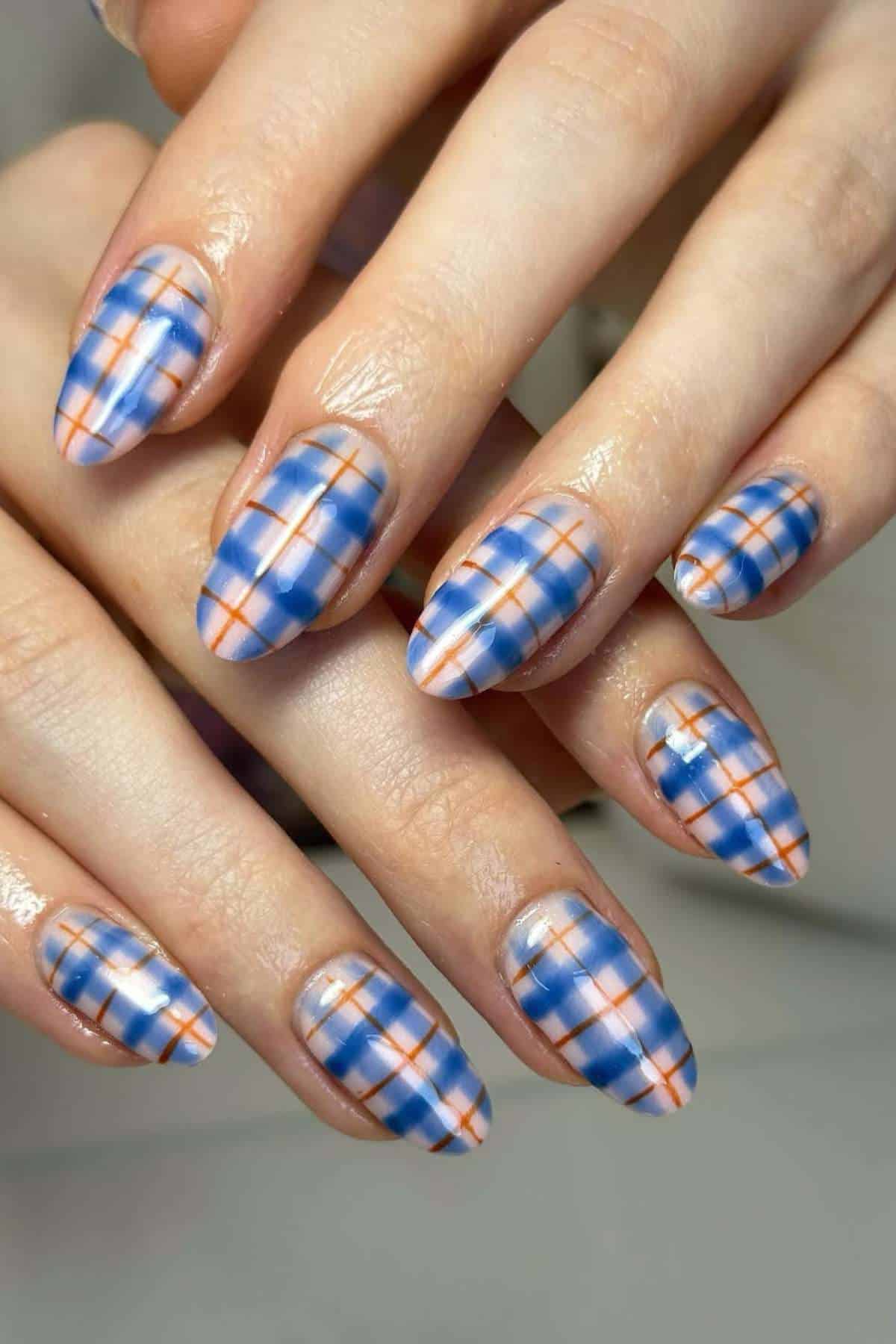 Close-up of hands with almond-shaped nails featuring a blue and orange plaid pattern on a translucent base.