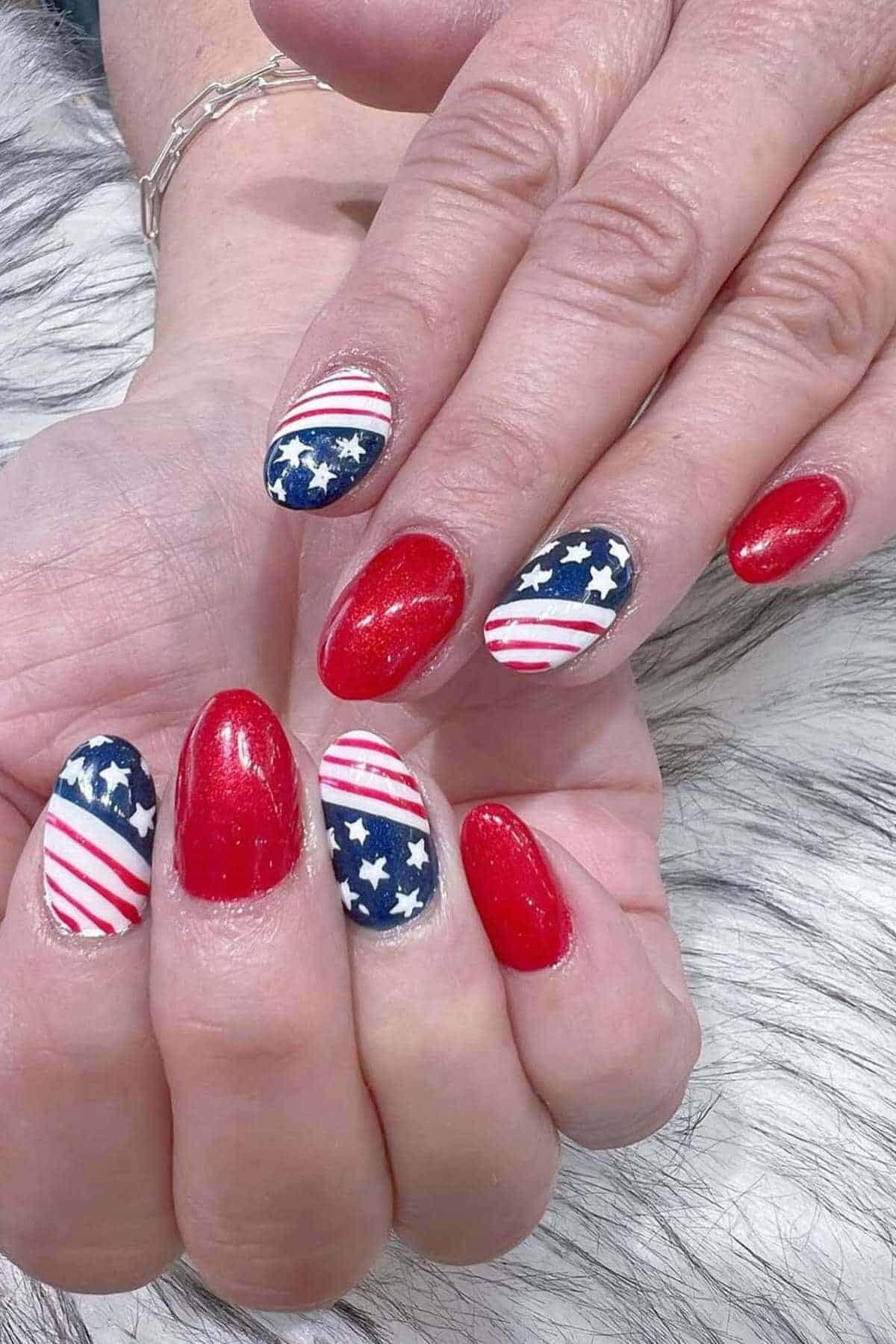 Close-up of hands with manicured nails painted in red, white, and blue with stars and stripes resembling the American flag.