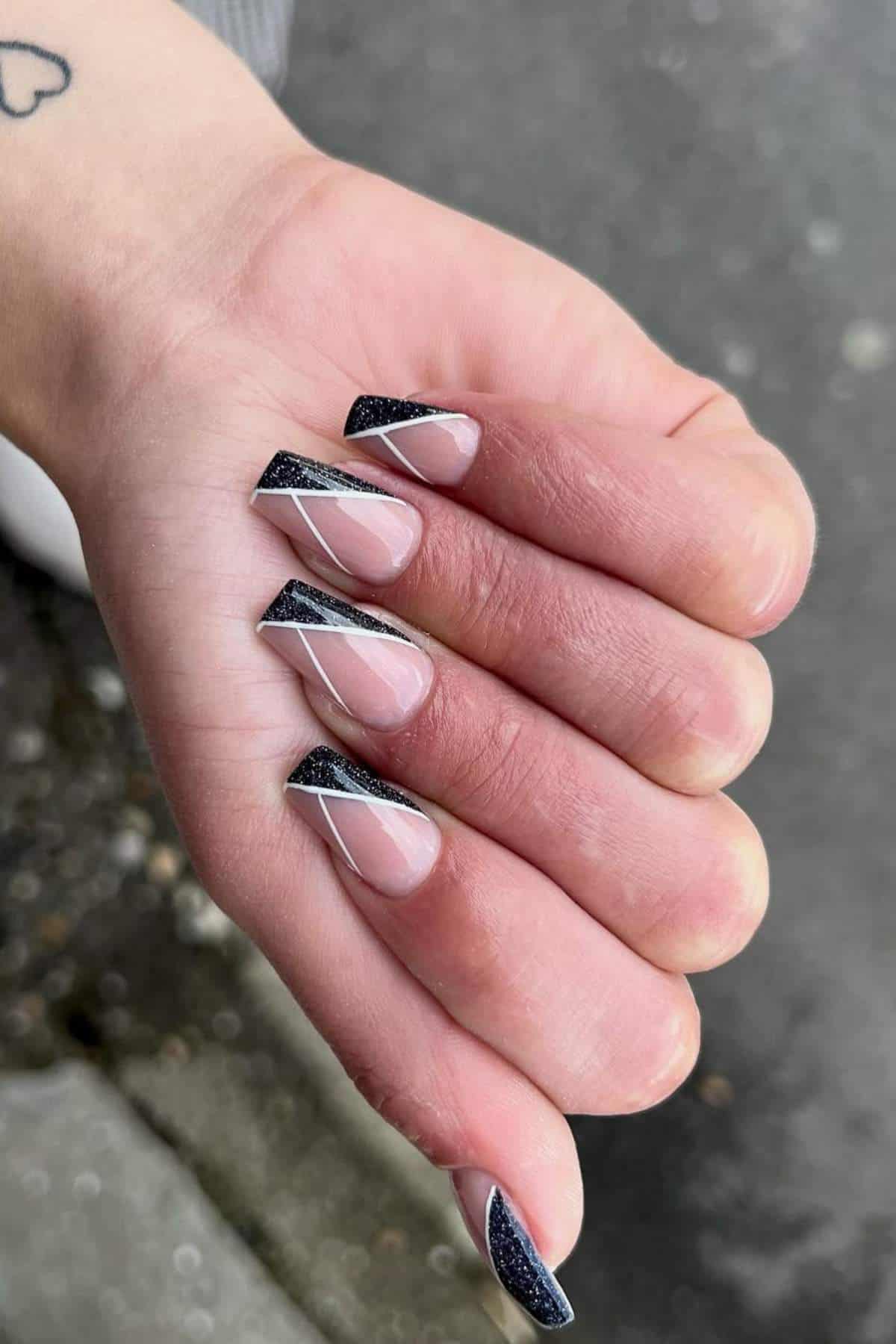 A hand with long coffin-shaped nails featuring a black and silver geometric design on a nude base.
