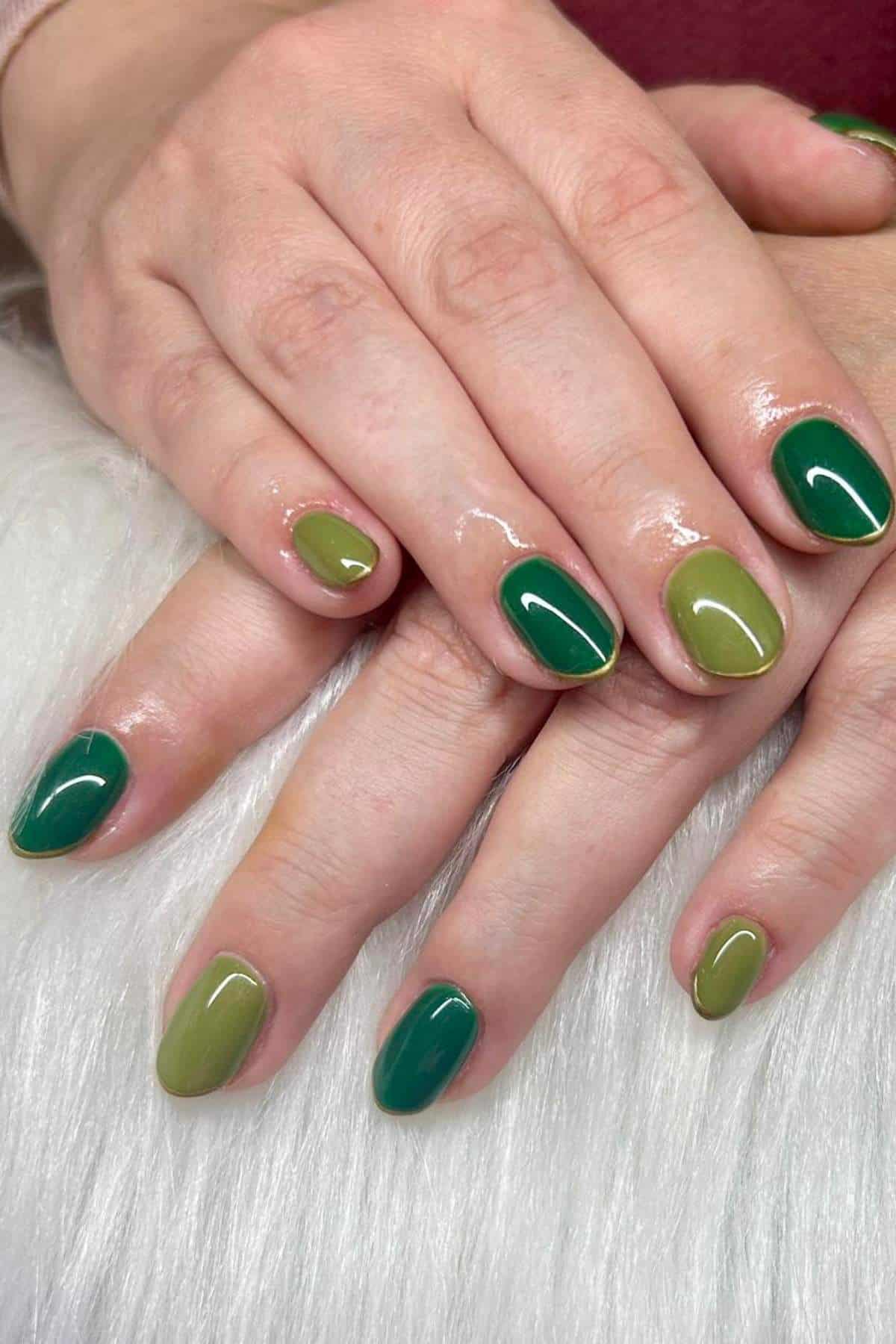 A close-up of hands with nails painted in alternating shades of green, resting on a white textured surface.