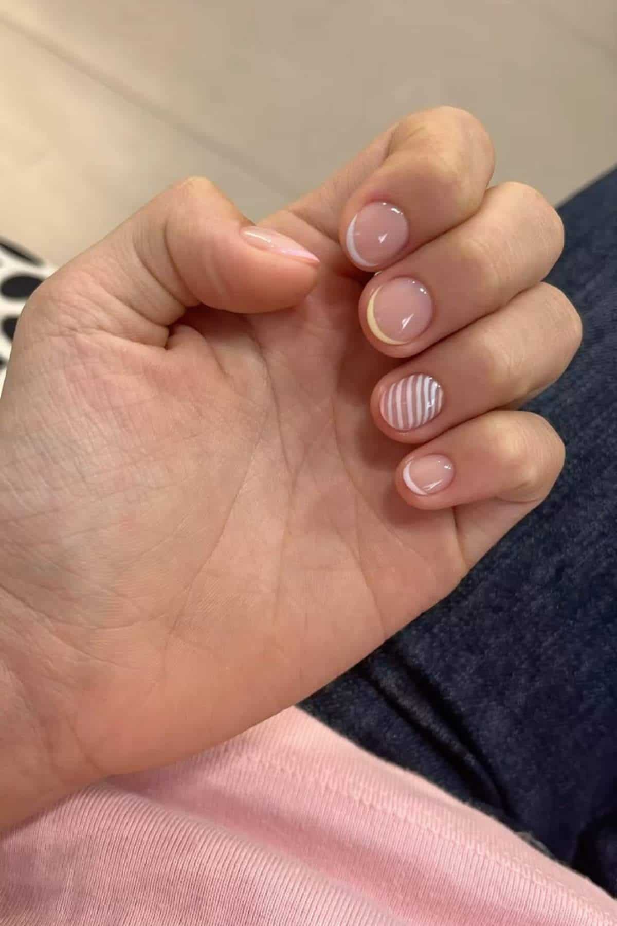 A hand with short, natural-looking nails; all nails are clear except the ring finger, which has white horizontal stripes on a clear base.