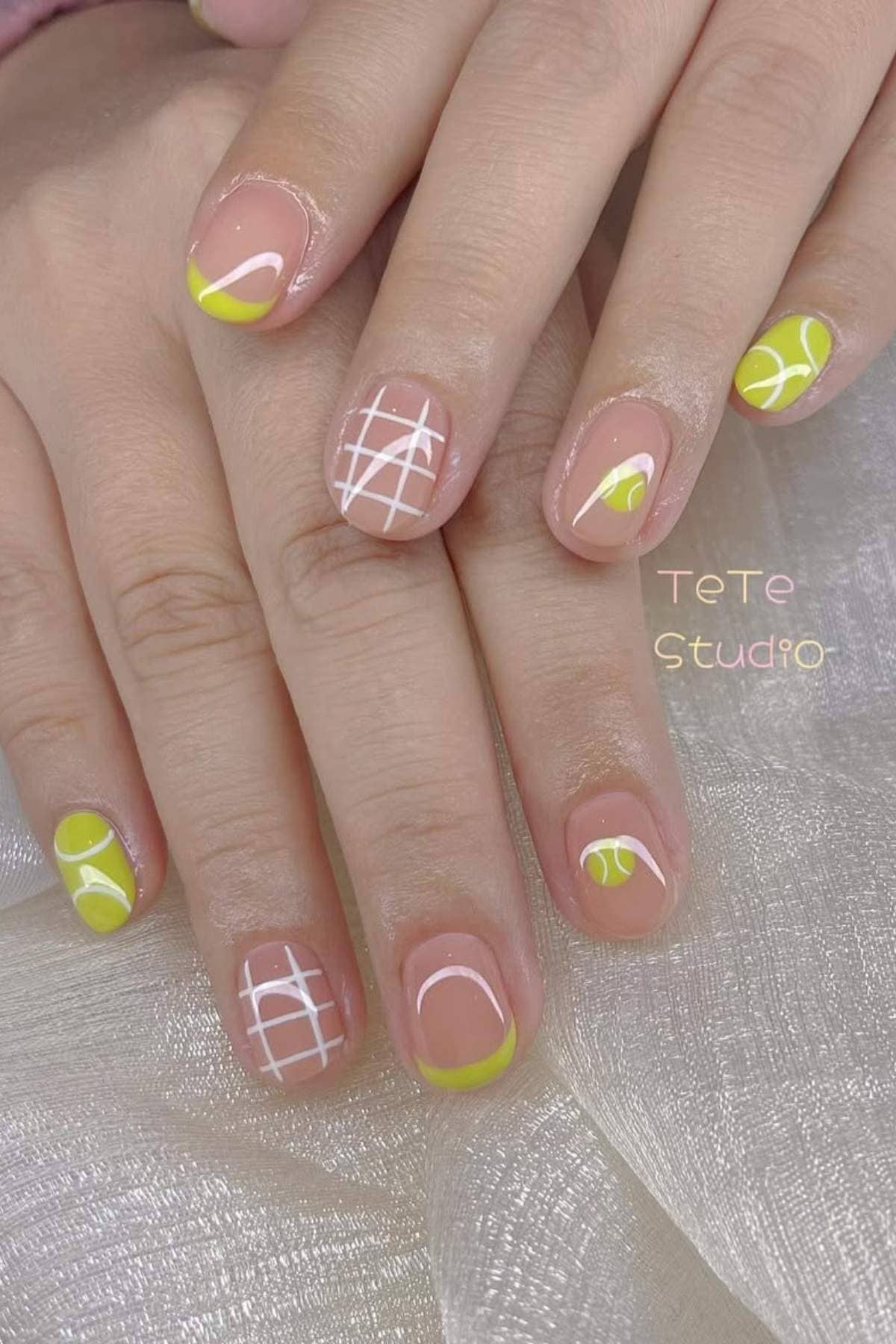 Fingernails with tennis-themed nail art, featuring neon yellow tips, white lines resembling tennis court markings, and tennis ball designs on a natural base.