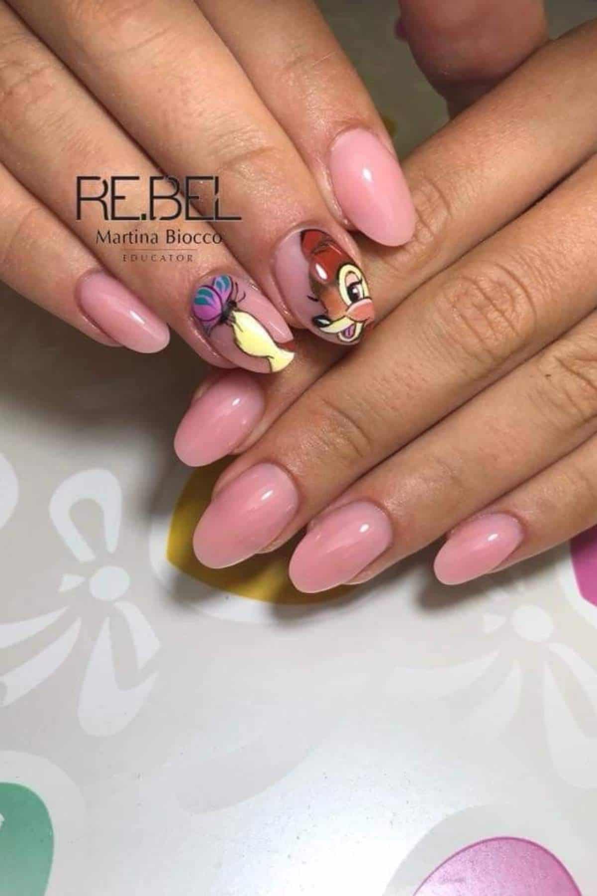 Hands with almond-shaped, glossy pink nails; two accent nails feature detailed cartoon character art with vibrant colors.