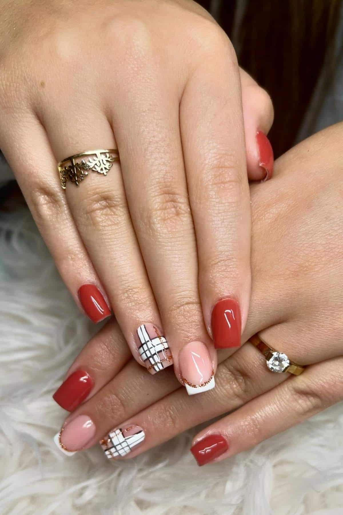 Hands with red and nude square-shaped nails, featuring accent nails with black and white plaid nail art. Gold rings are worn on two fingers.