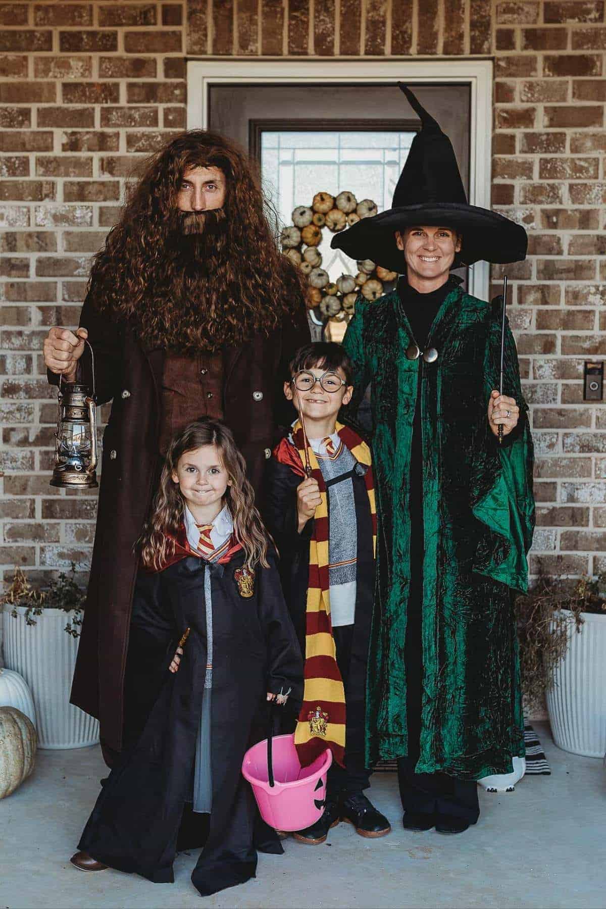 Four people dressed as Harry Potter characters pose in front of a brick house. An adult is Hagrid, another is McGonagall, and two children are dressed as Hermione and Harry Potter.