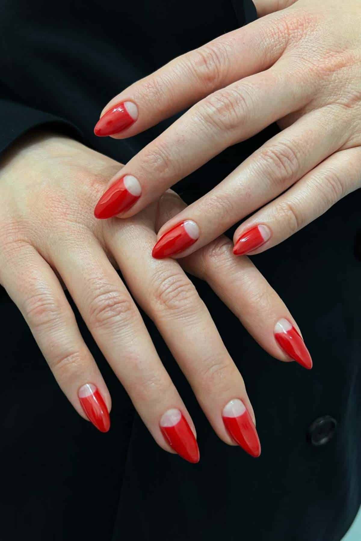 Hands with almond-shaped nails painted red, featuring a half-moon design at the base near the cuticles.