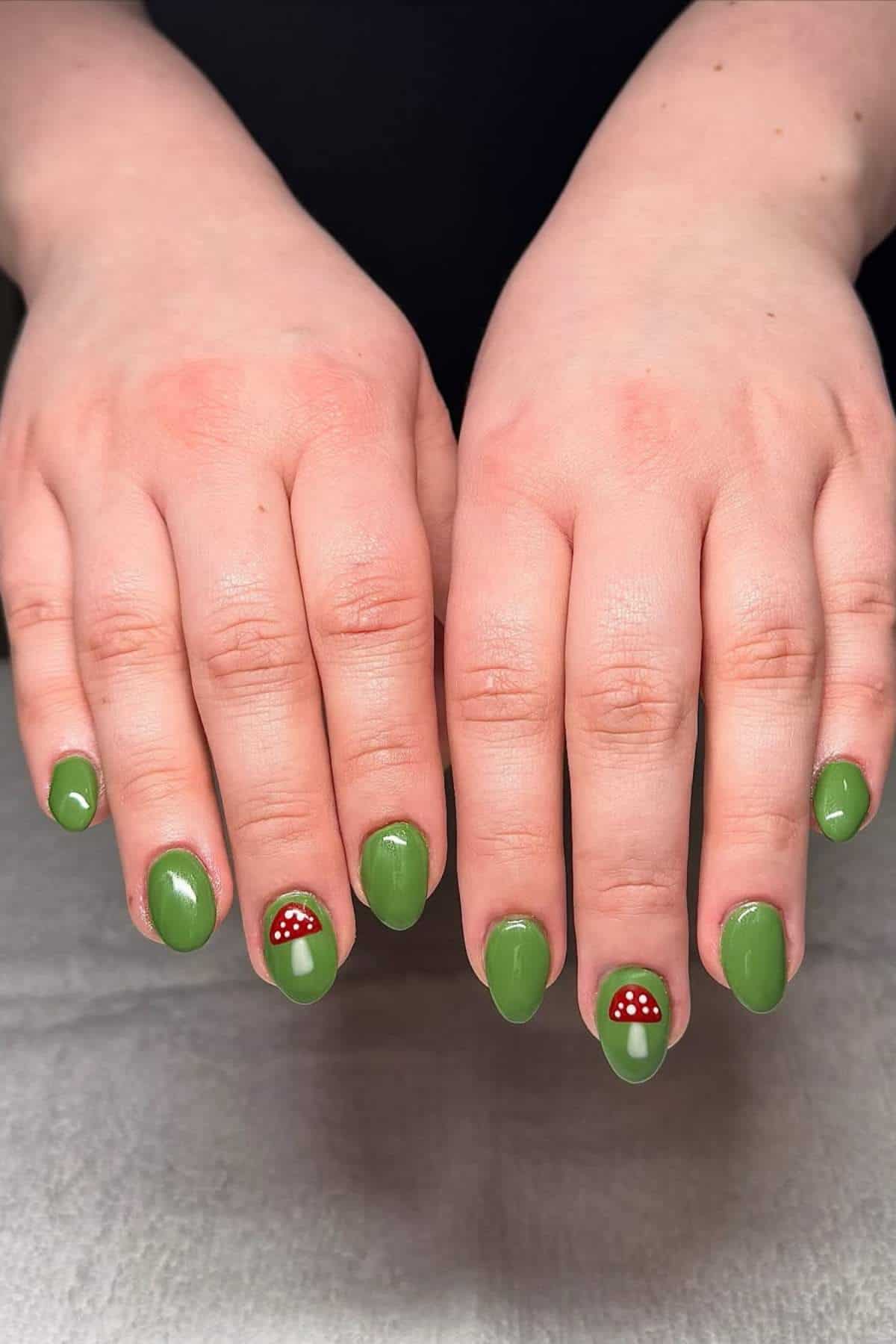Two hands with green nail polish; ring fingernails feature a red and white mushroom design.