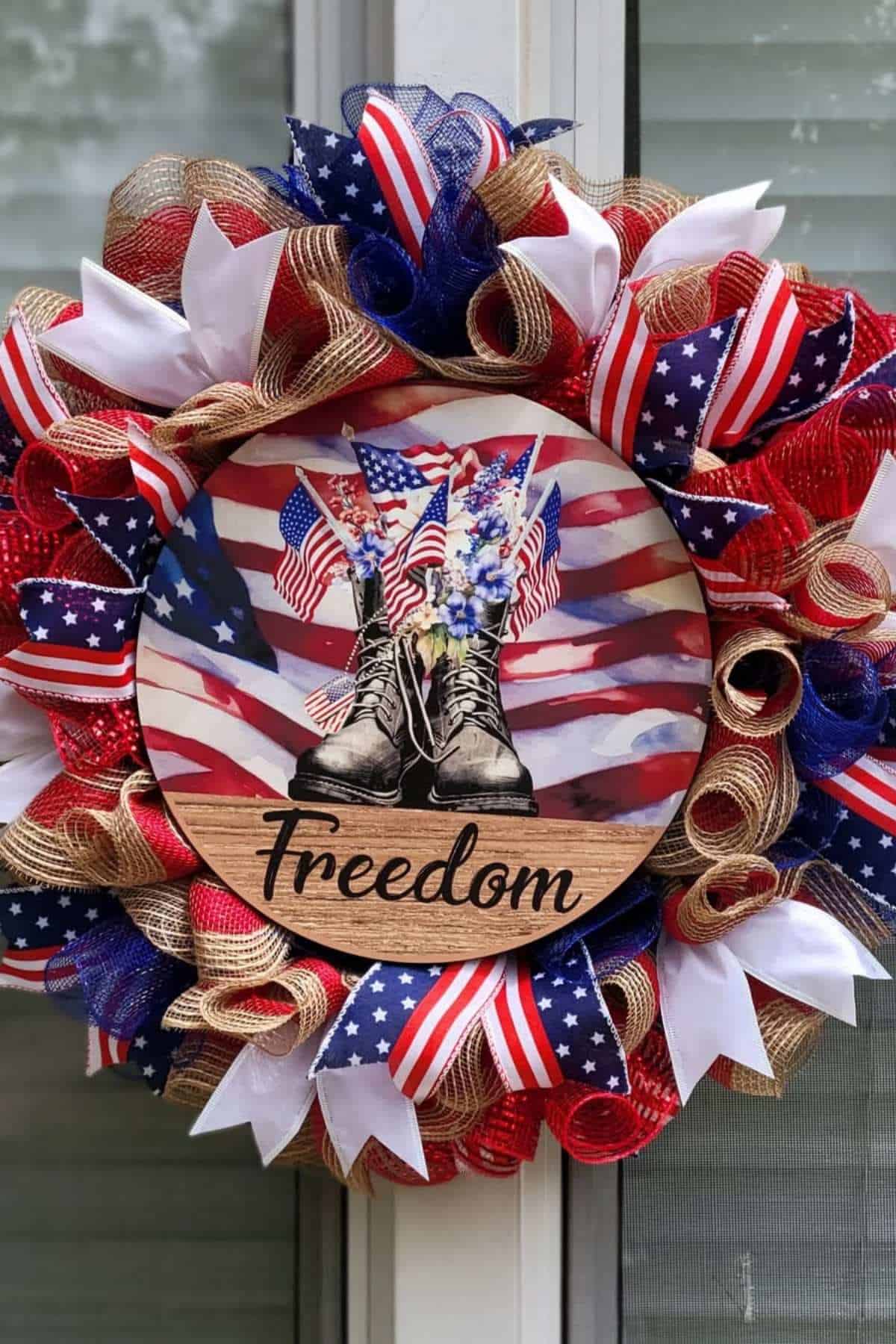 Patriotic wreath with red, white, and blue ribbons, a central sign showing boots, American flags, flowers, and the word "Freedom.