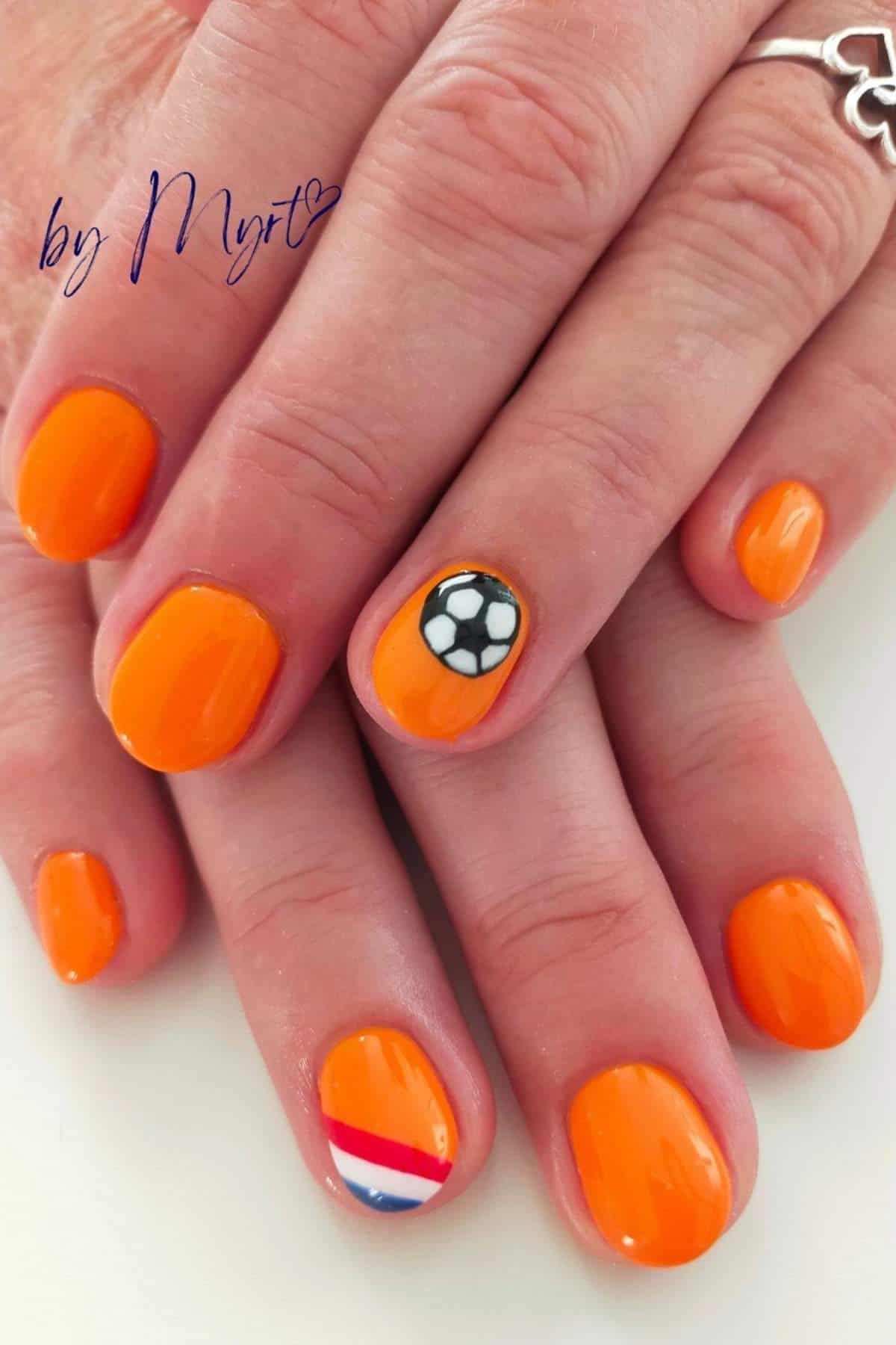 Hands with orange nail polish; one nail features a soccer ball design and another displays a red, white, and blue stripe.