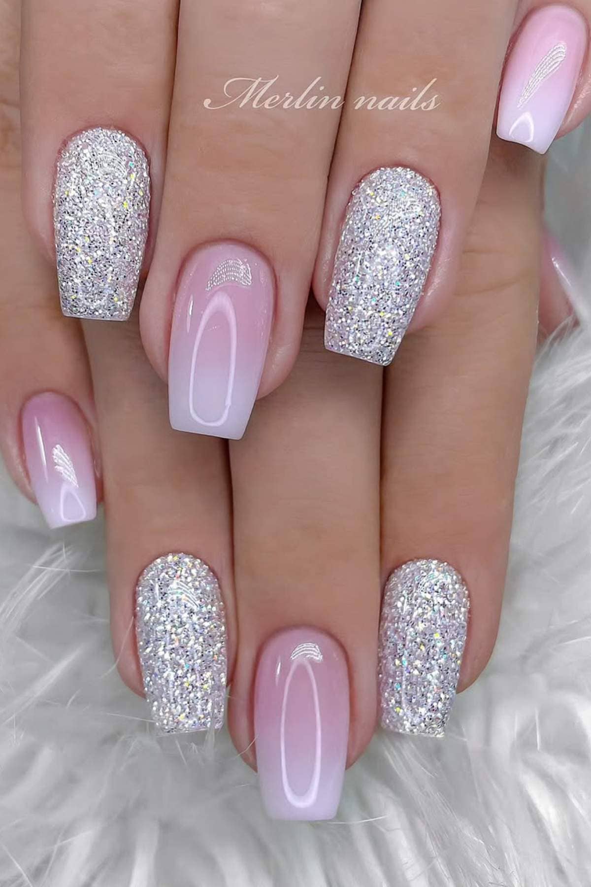 A hand with square-shaped nails featuring a pink ombre and accent nails covered in silver glitter polish.