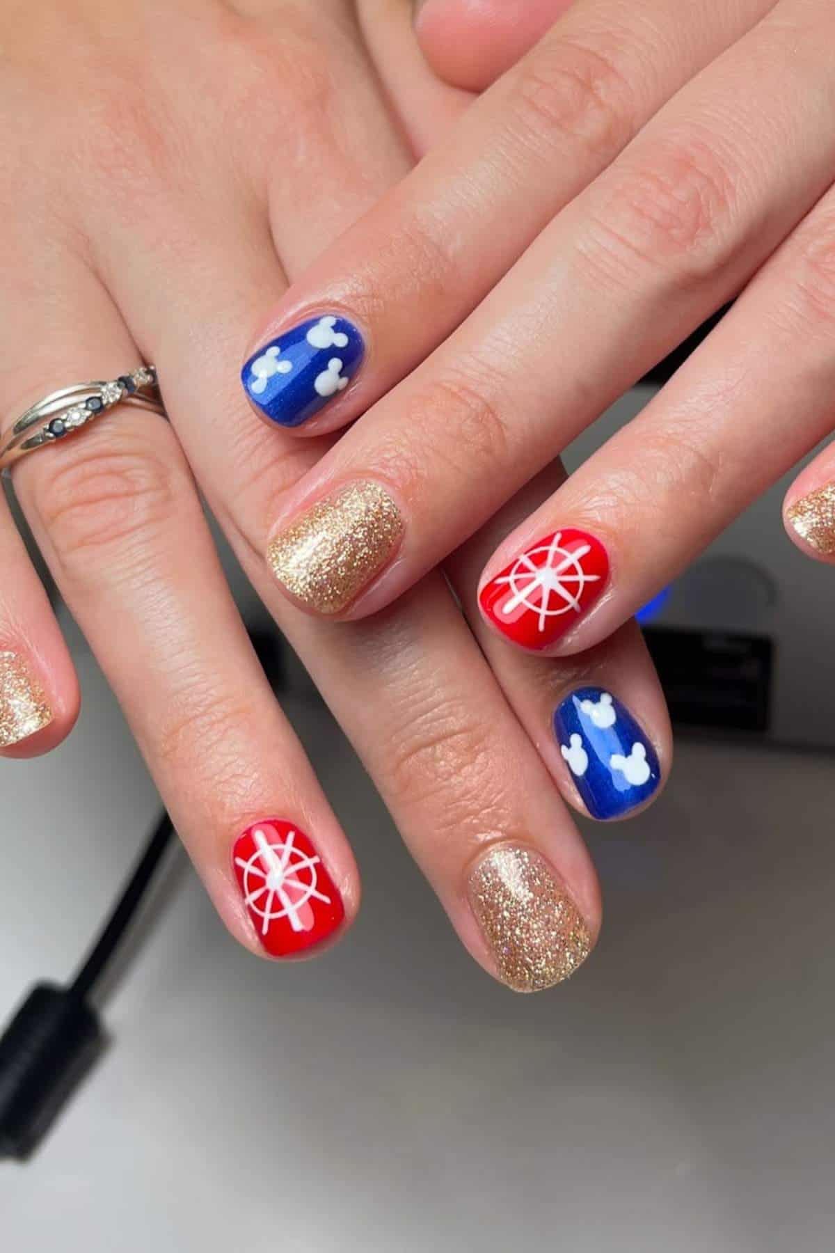 Fingernails with gold glitter polish, red polish with white compass designs, and blue polish with white cloud shapes.