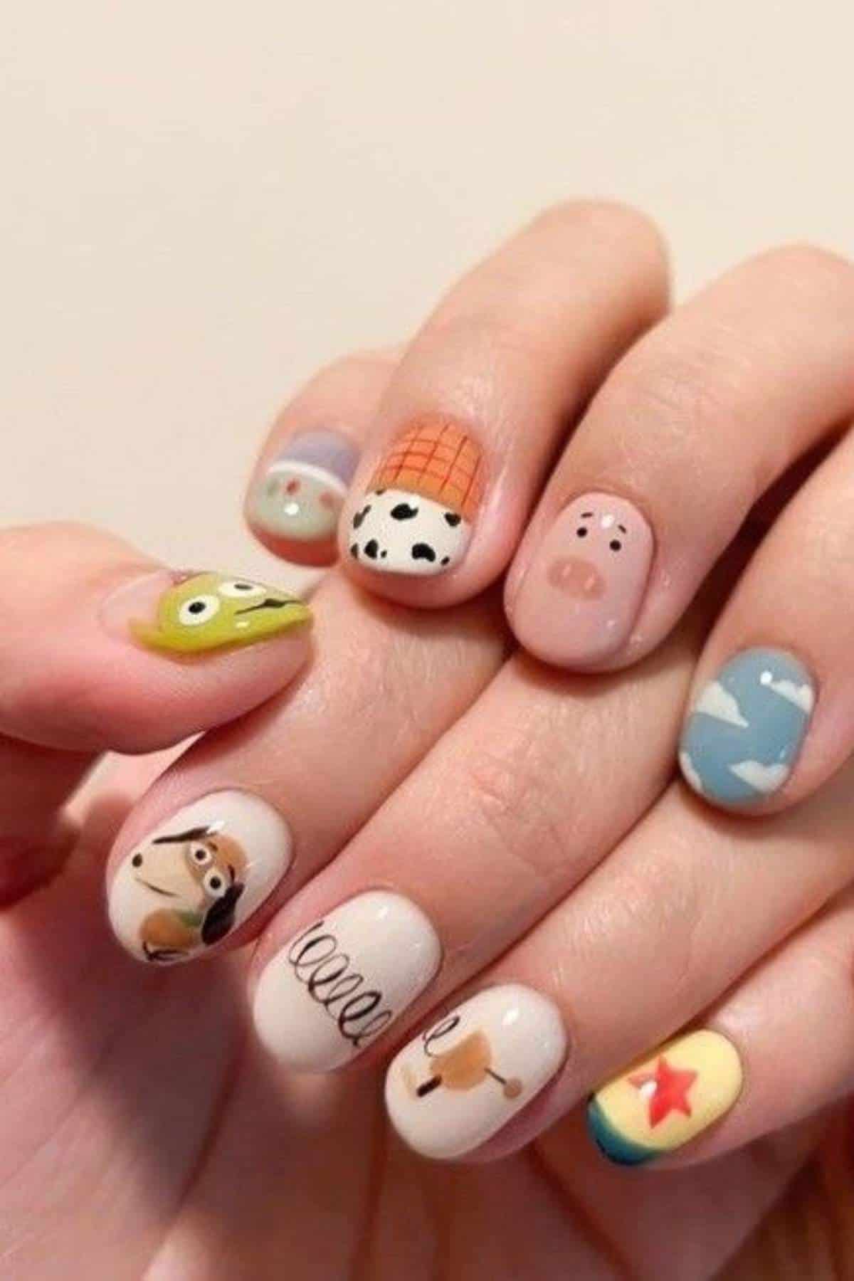 Hands with short nails painted with Toy Story character designs and motifs, including Woody, Buzz, Jessie, Rex, clouds, a pig, and the Pixar ball.