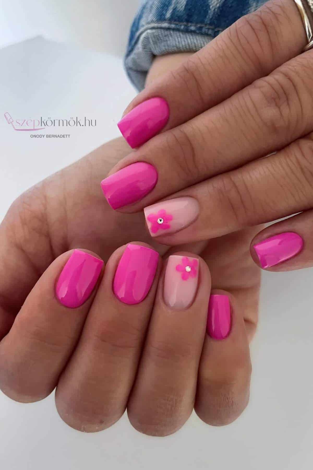 Close-up of hands with pink manicured nails; two nails feature a light pink base and small flower decorations.