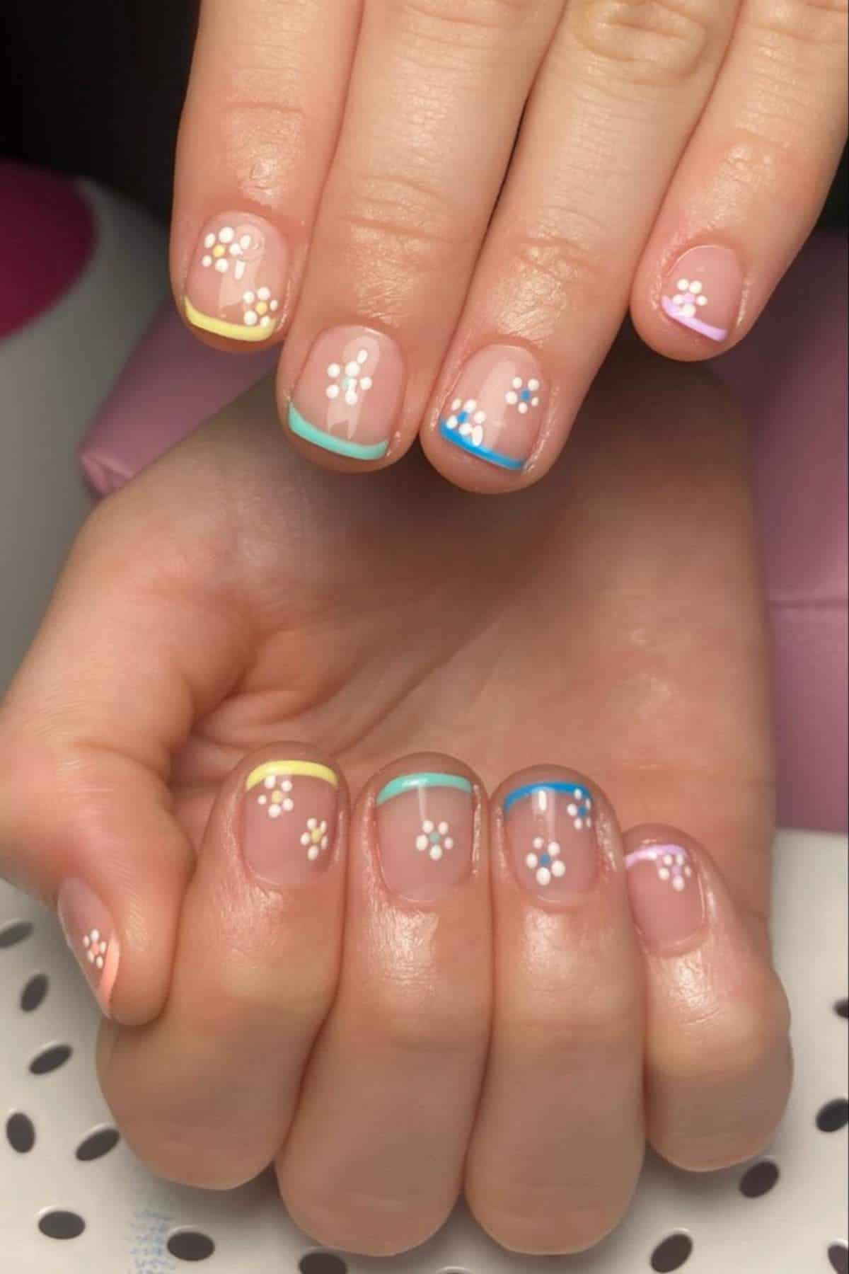Hands with a manicure featuring pastel French tips and small white flower designs on clear nails.
