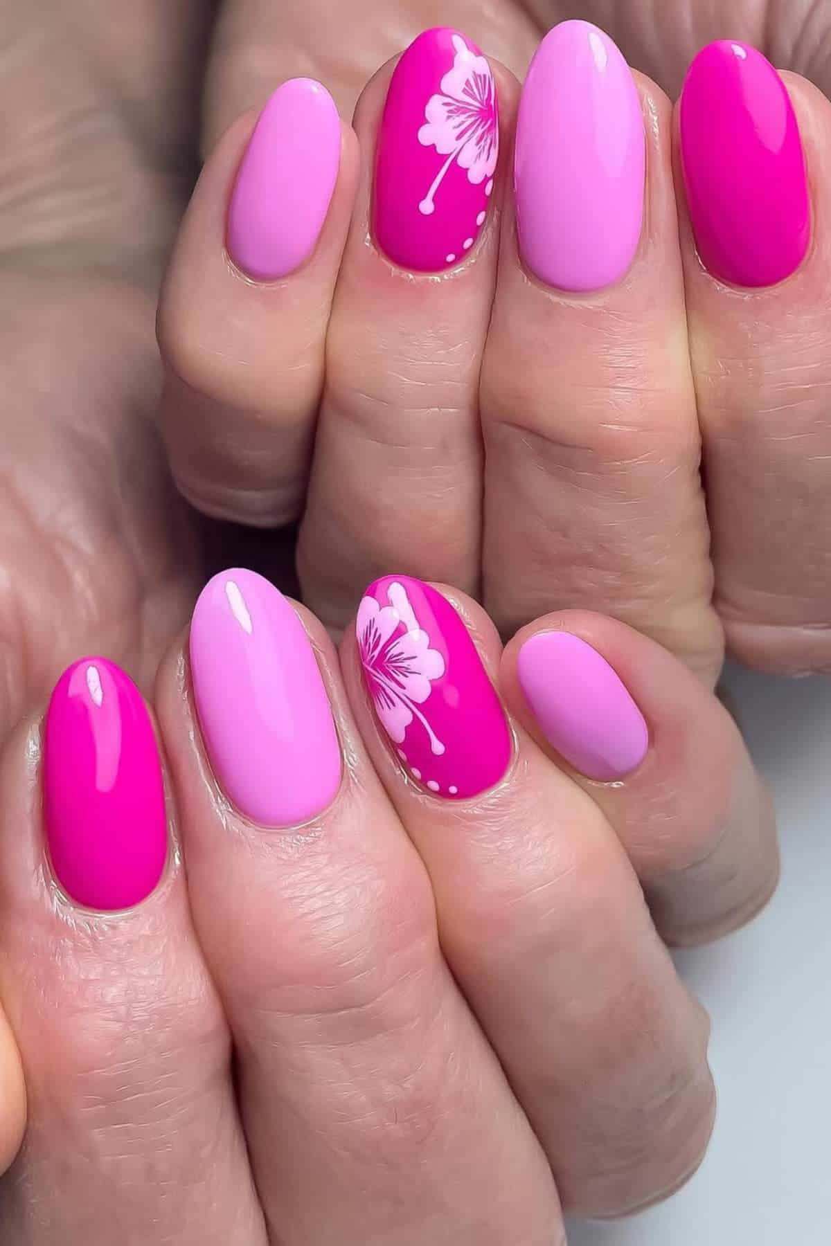 Close-up of hands with pink and magenta manicured nails; two nails feature a white floral design and small white dots.
