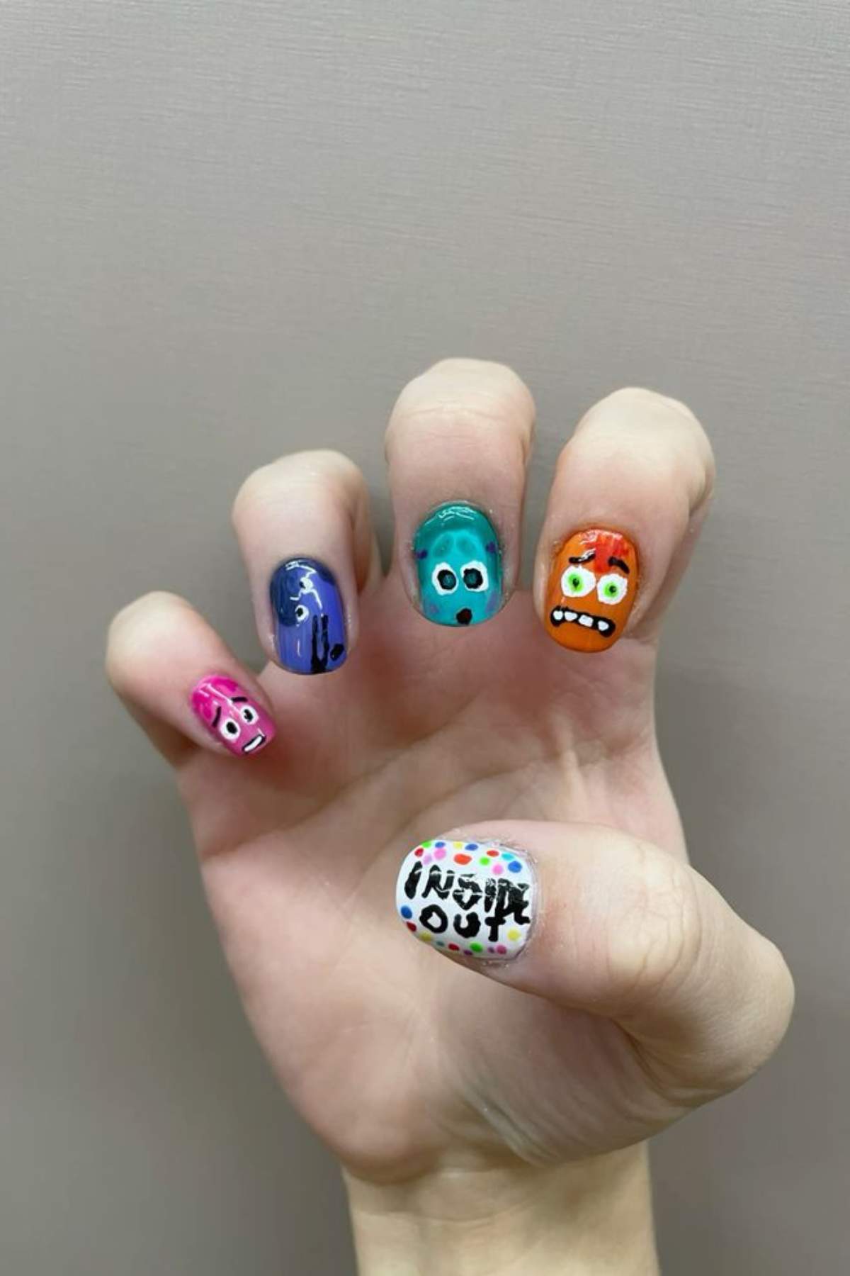 A hand with fingernails painted with cartoon character faces and the words "Inside Out" on the thumb, referencing the animated movie.