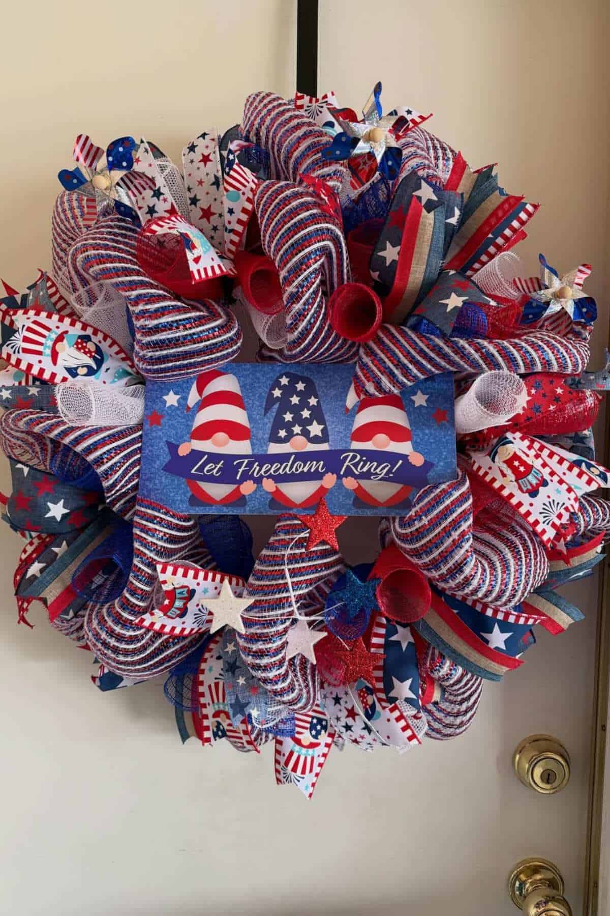Patriotic wreath with red, white, and blue ribbons, stars, and a sign reading "Let Freedom Ring!" hanging on a door.