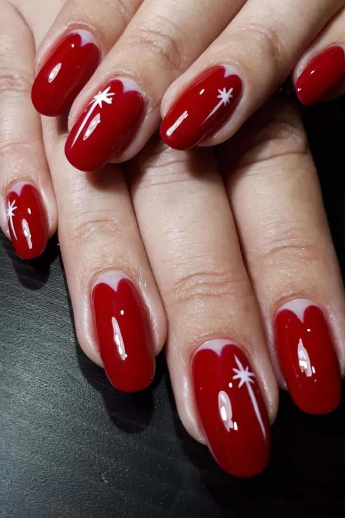 Hands with short, oval-shaped nails painted glossy red; two nails feature a small white starburst design near the tips.