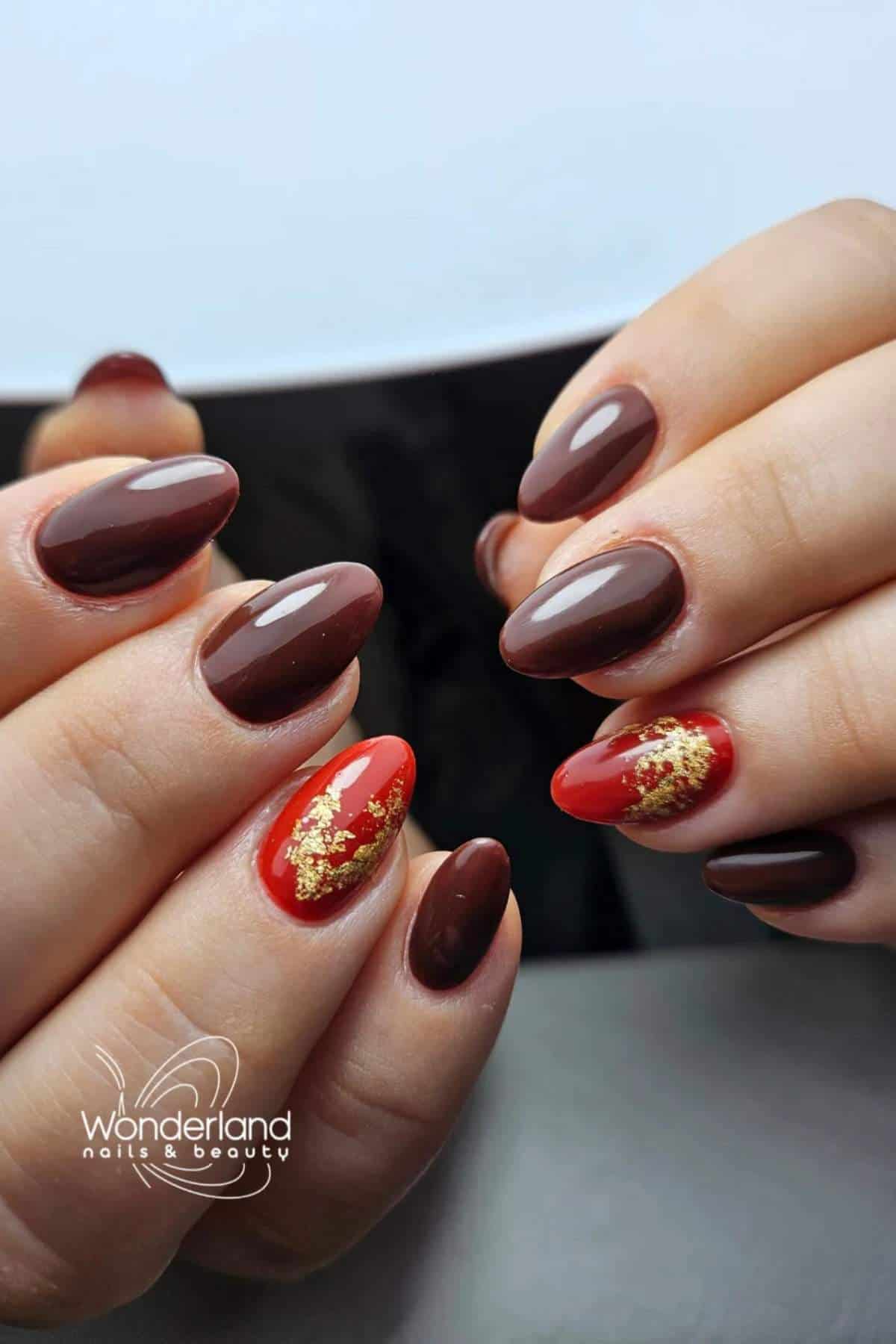 Close-up of hands with glossy brown manicure; ring fingers feature red polish with gold foil accents. Logo "Wonderland nails & beauty" is visible in the corner.