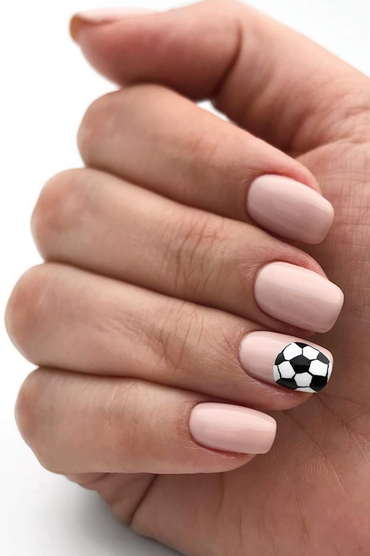 A hand with short, light pink manicured nails; the ring fingernail features a black and white soccer ball design.