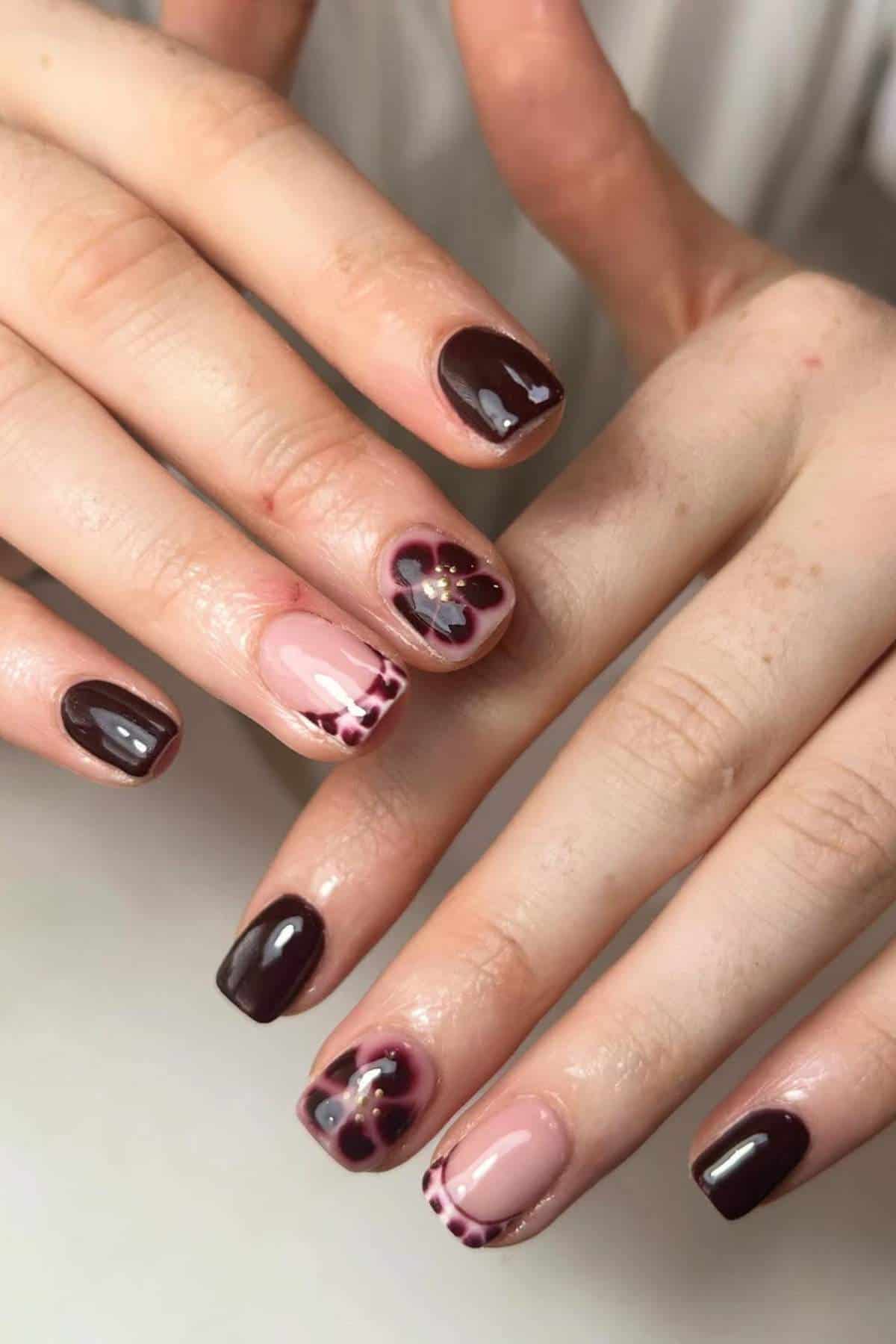 Close-up of hands with manicured nails; nails are painted dark burgundy and light pink with floral and dotted designs on some nails.