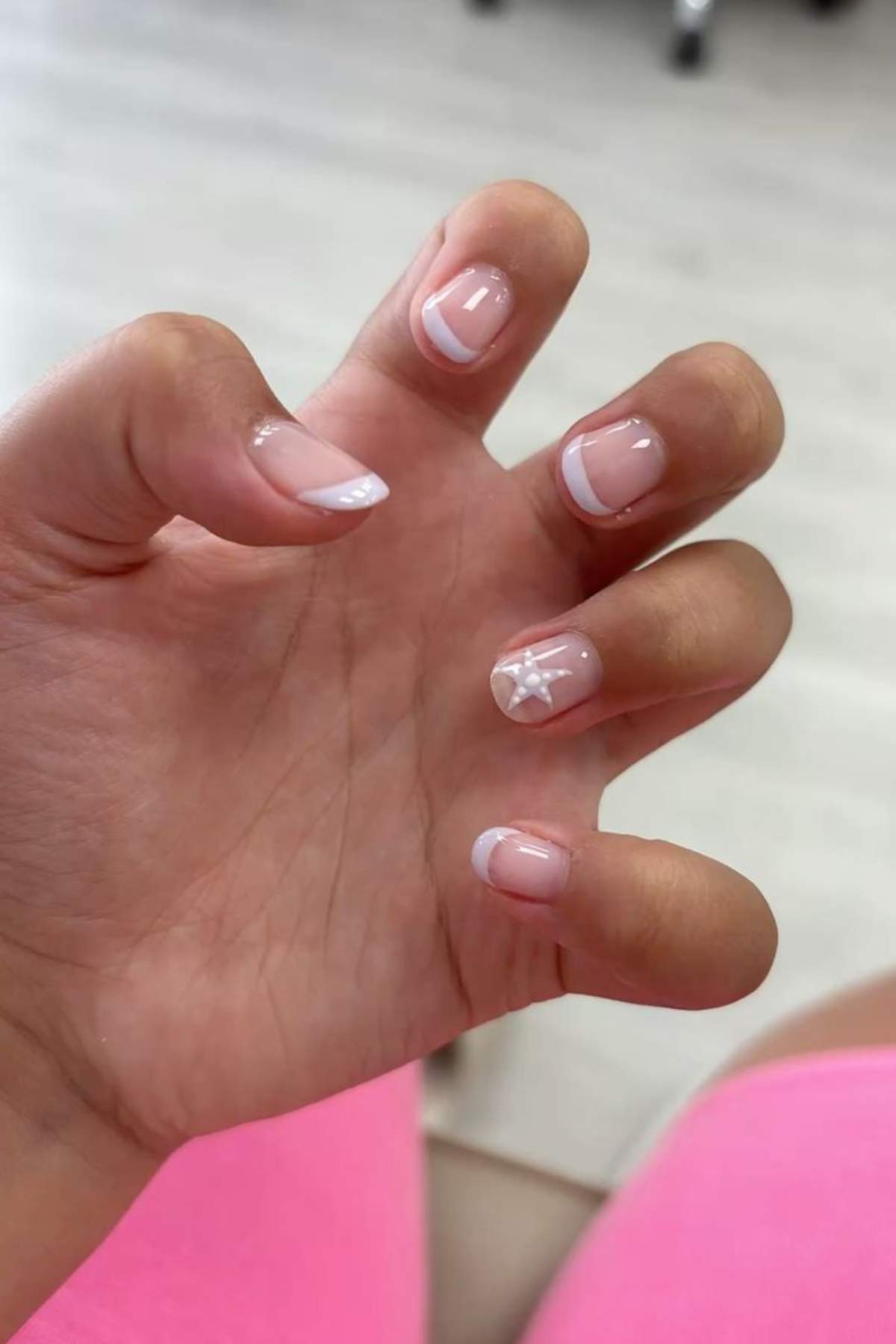 A hand with a French manicure, featuring white tips and a small white flower design on the ring fingernail.
