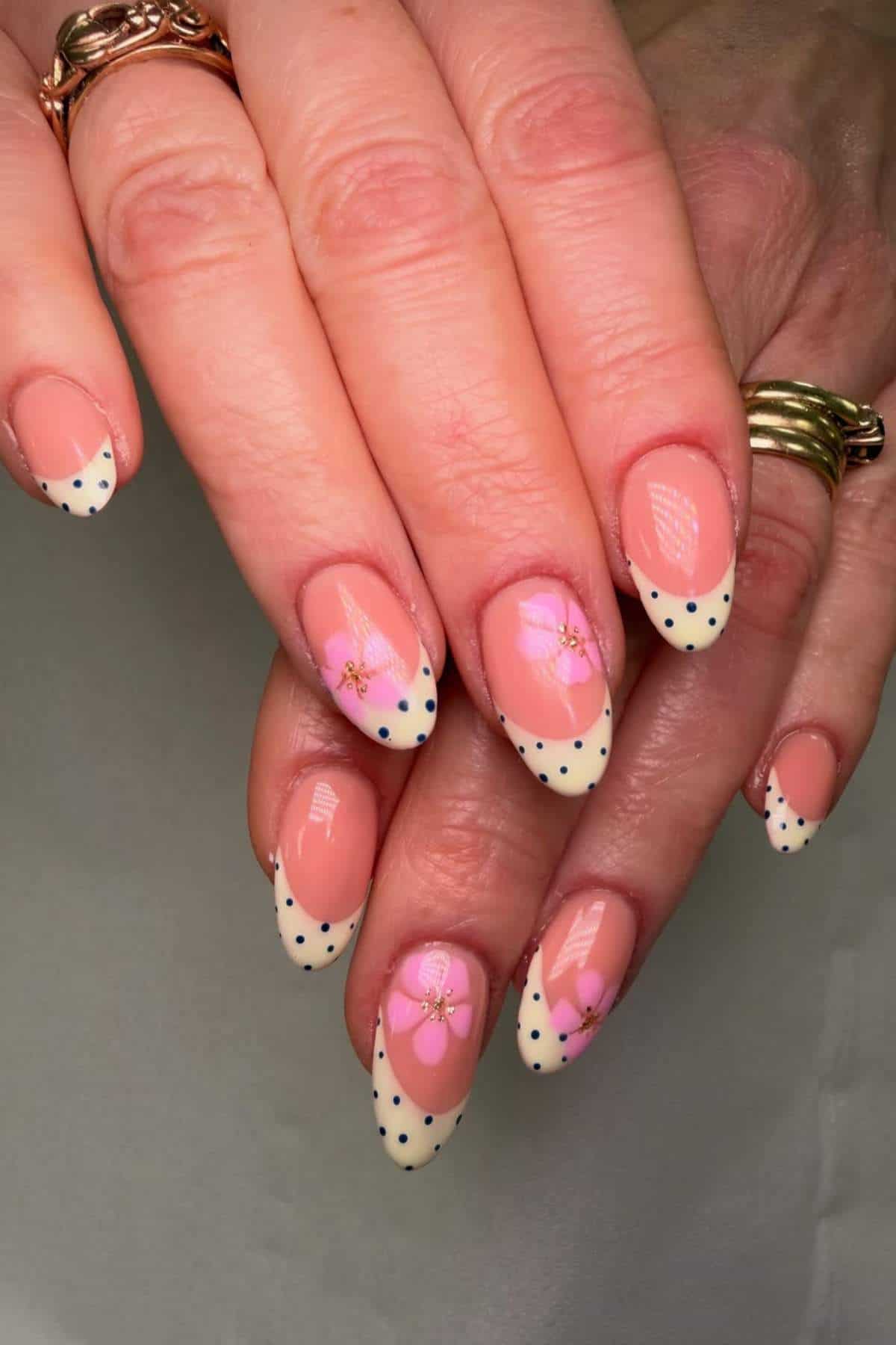 A hand with almond-shaped nails featuring cream tips with navy polka dots and pink floral designs on a natural pink base.