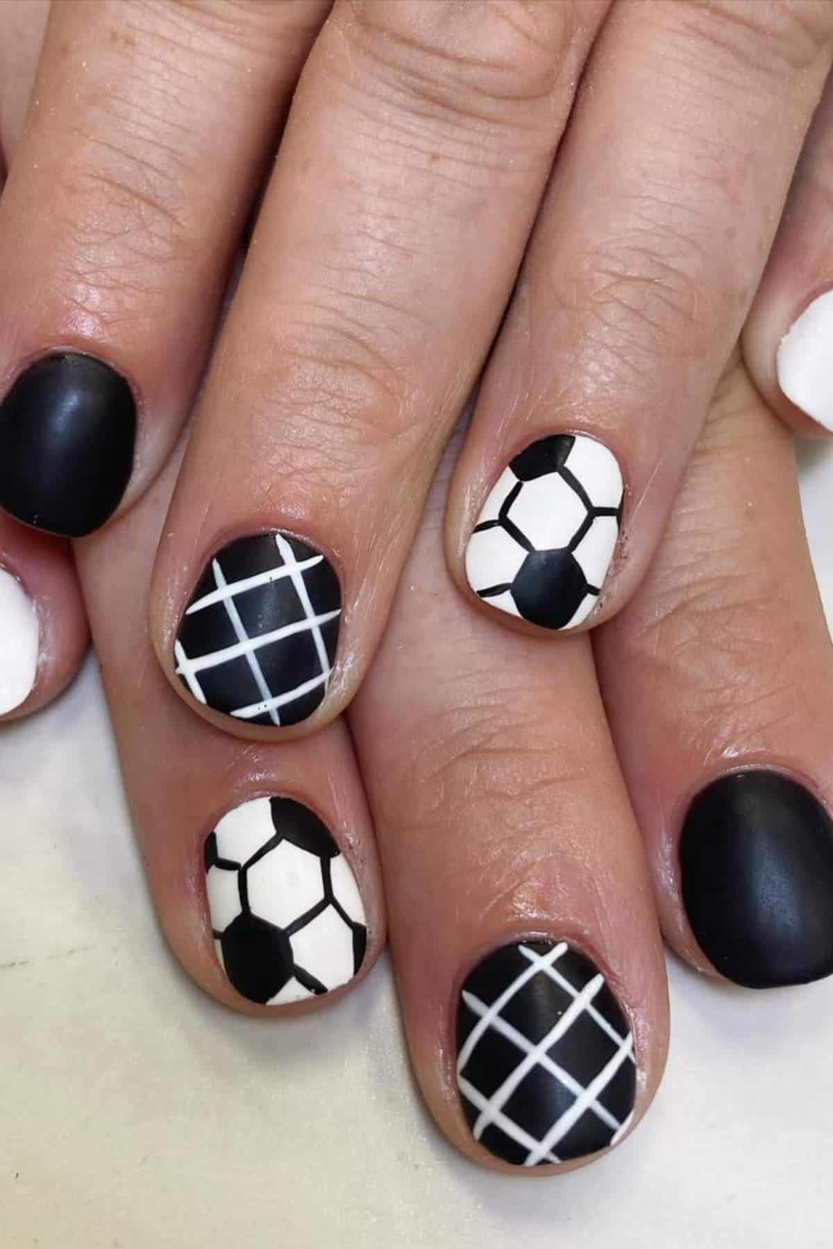 A hand with nails painted in black and white, featuring designs resembling soccer balls and net patterns.