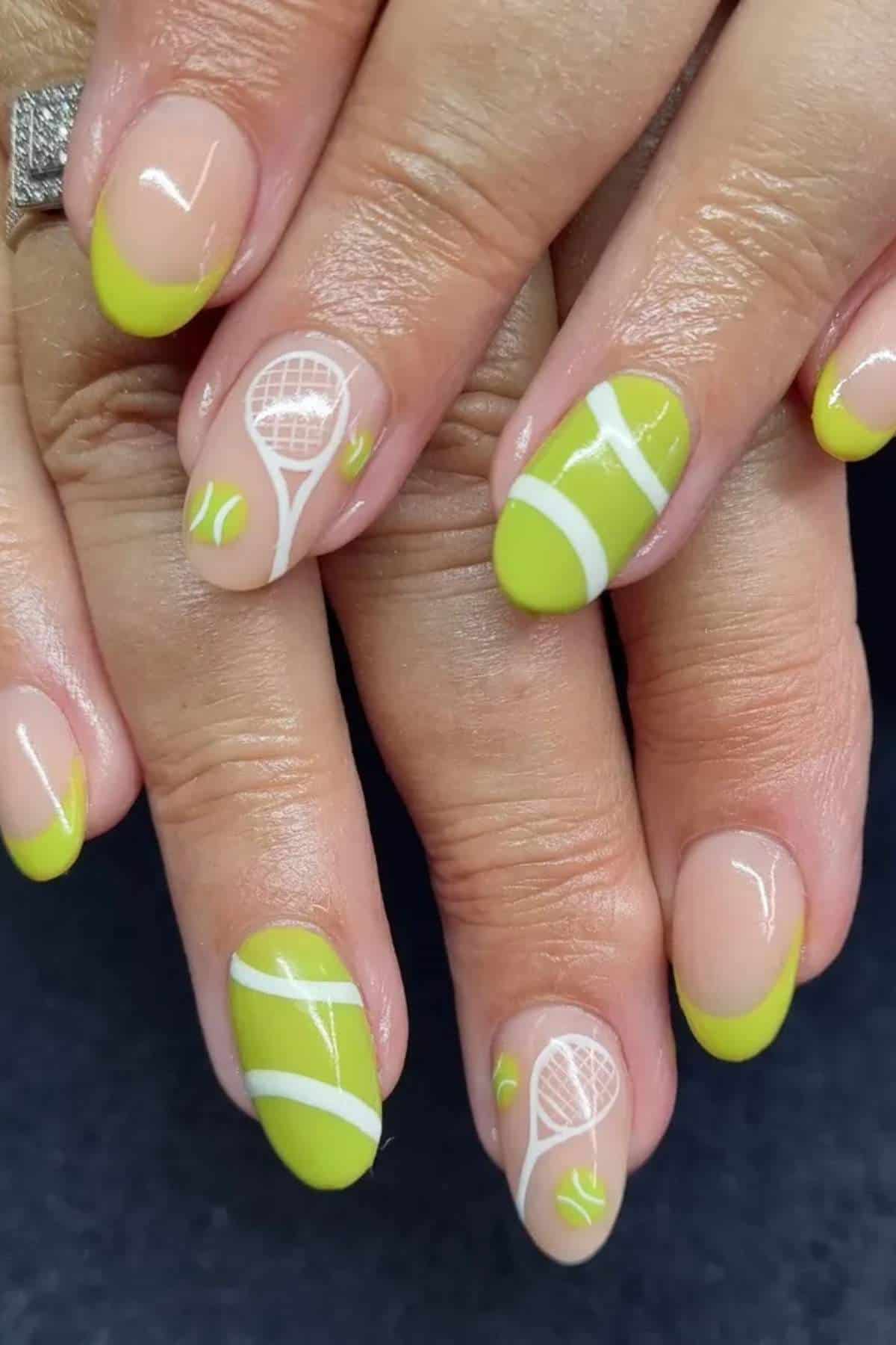 Fingernails painted with lime green French tips and tennis-themed designs, including tennis balls, rackets, and white lines, on a dark background.