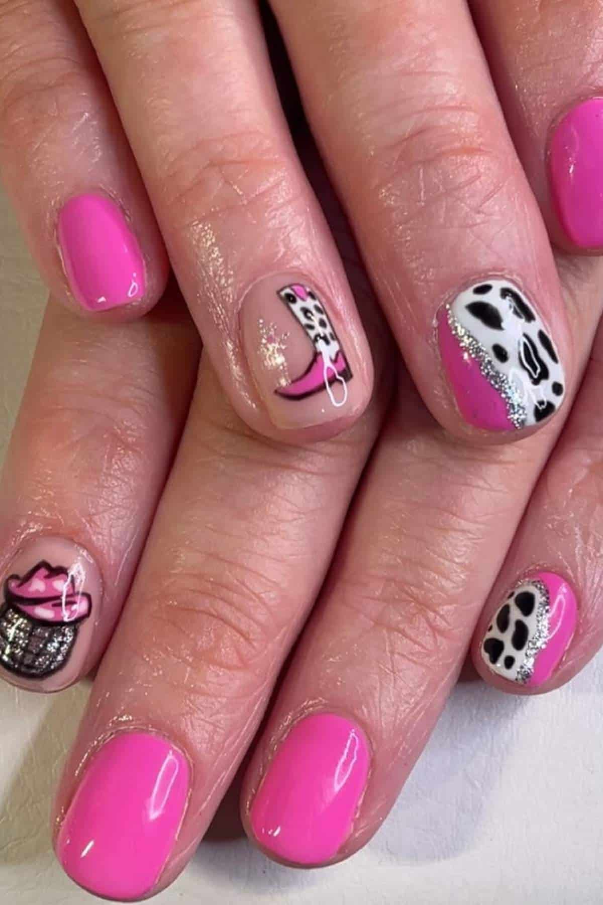 Hands with pink nail polish, featuring accent nails with black and white cow print designs, silver glitter, and a pink cowboy hat illustration.