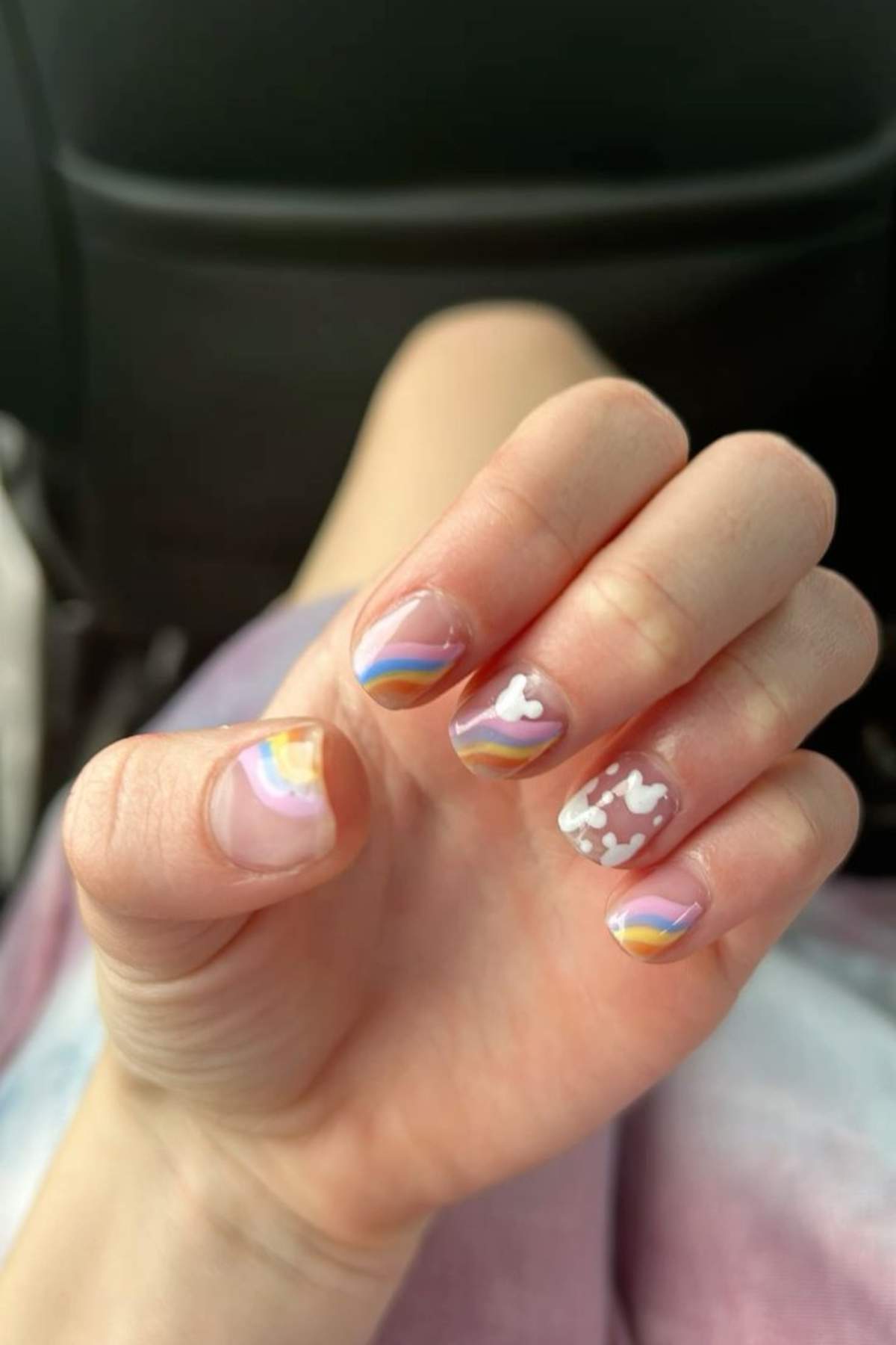 Close up of a person's hand with a manicure featuring rainbow and cloud designs on the nails.