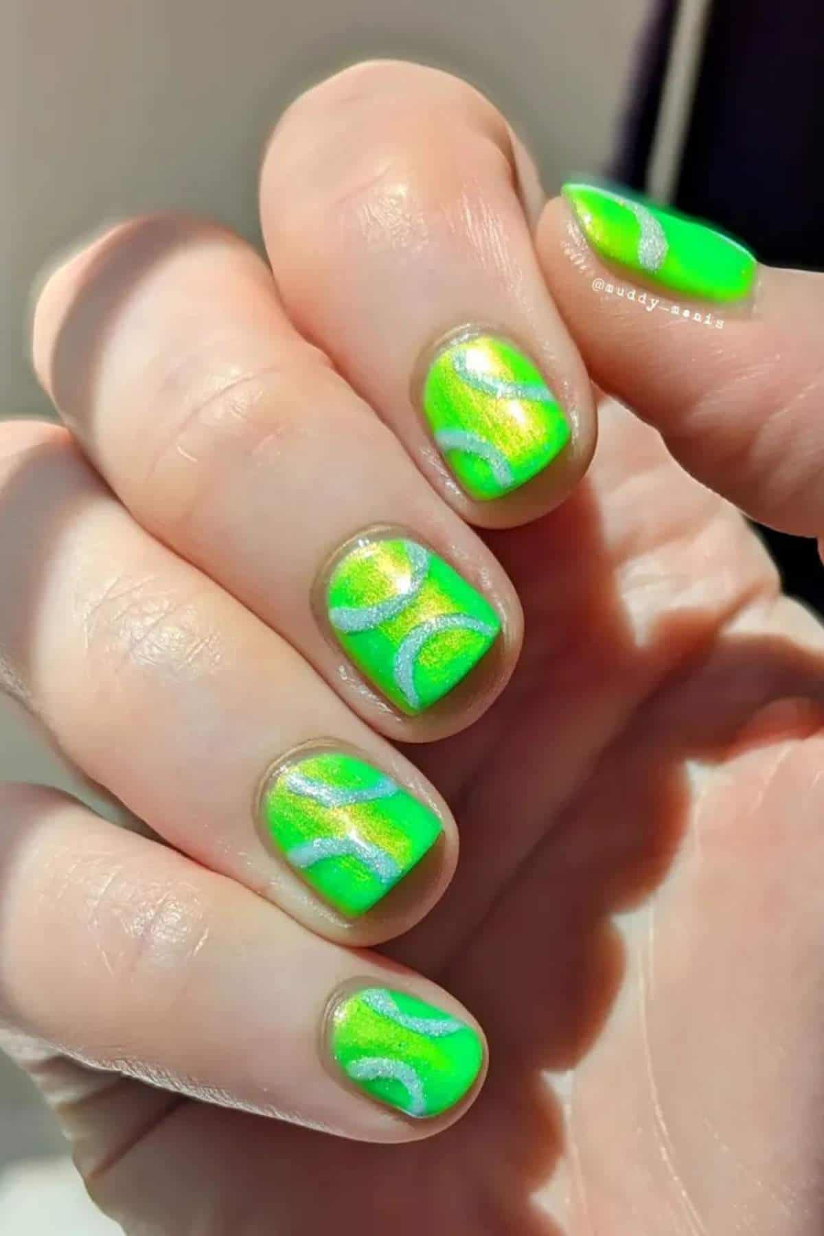 A hand with short nails painted neon green with iridescent silver wavy lines on each nail.