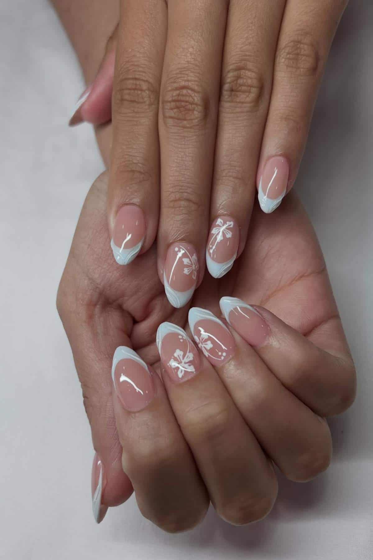 Hands with manicured nails featuring a French tip design and white floral accents on a few nails, displayed on a light background.