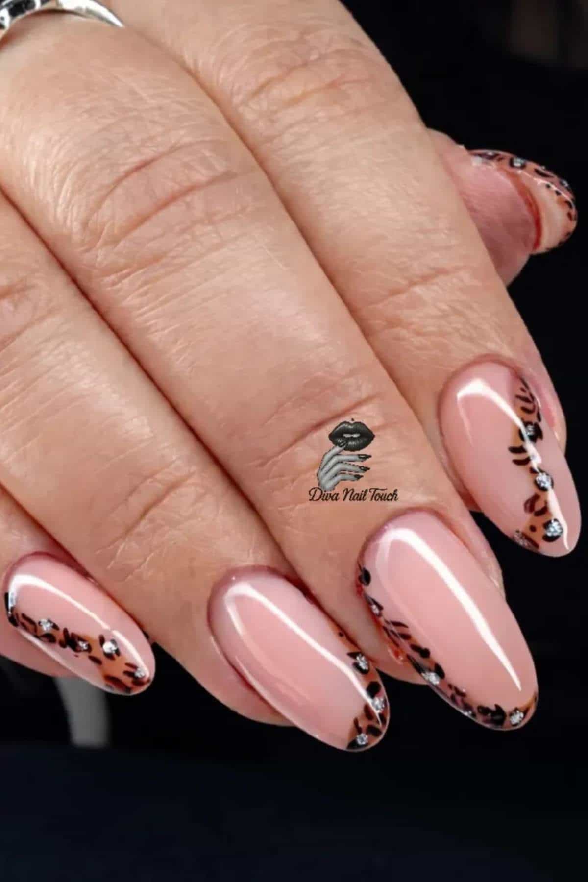 A hand with almond-shaped nails featuring a pink base and brown and black leopard print design on the tips.