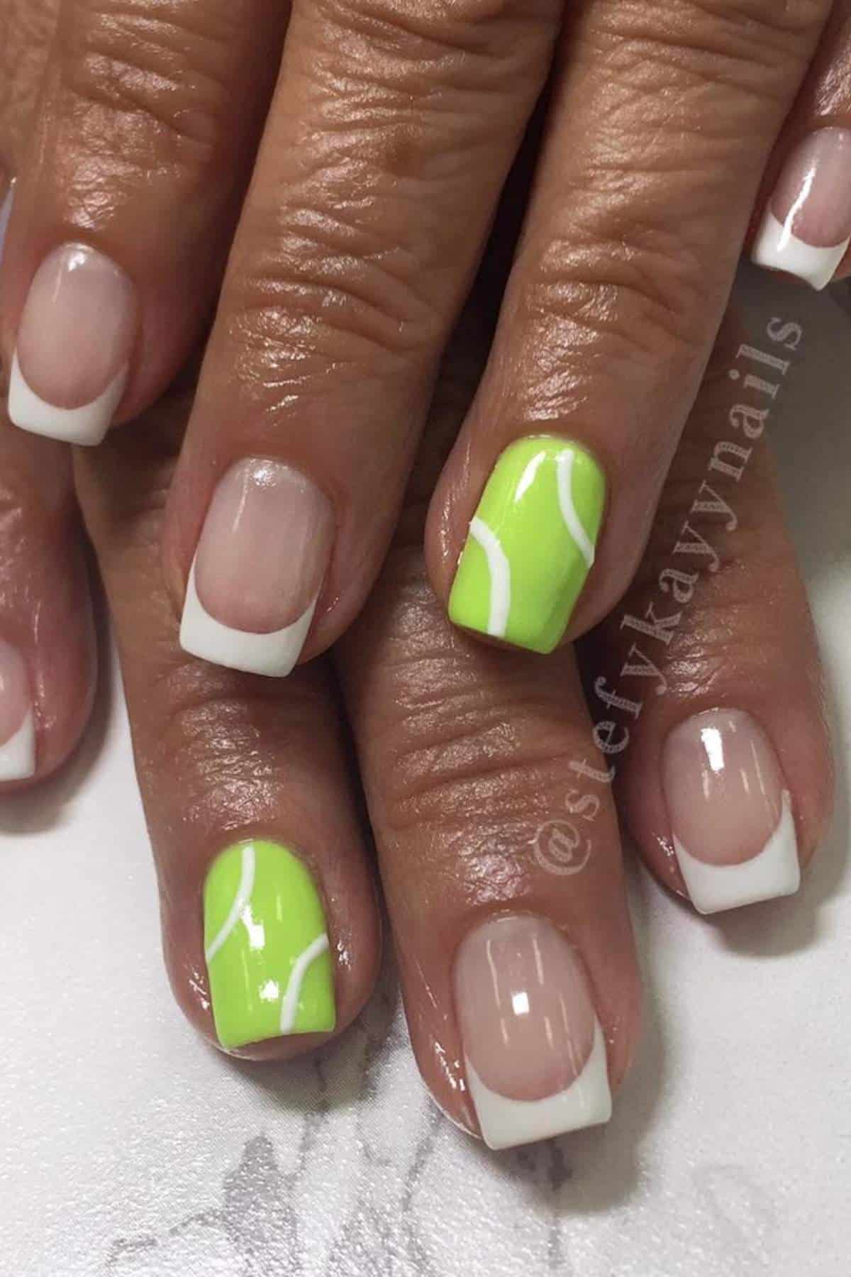 A hand with French manicured nails; two accent nails are painted bright green with white curved lines resembling tennis balls.