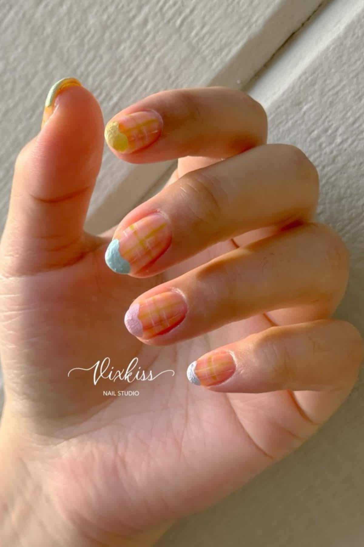 A hand with multicolored pastel nail art featuring abstract patterns and wavy tips, positioned against a neutral background.