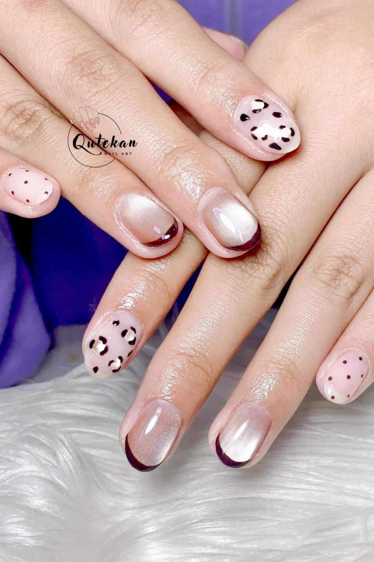 Hands with short nails featuring a mix of maroon French tips, polka dots, and abstract animal print designs on a glossy light pink base.