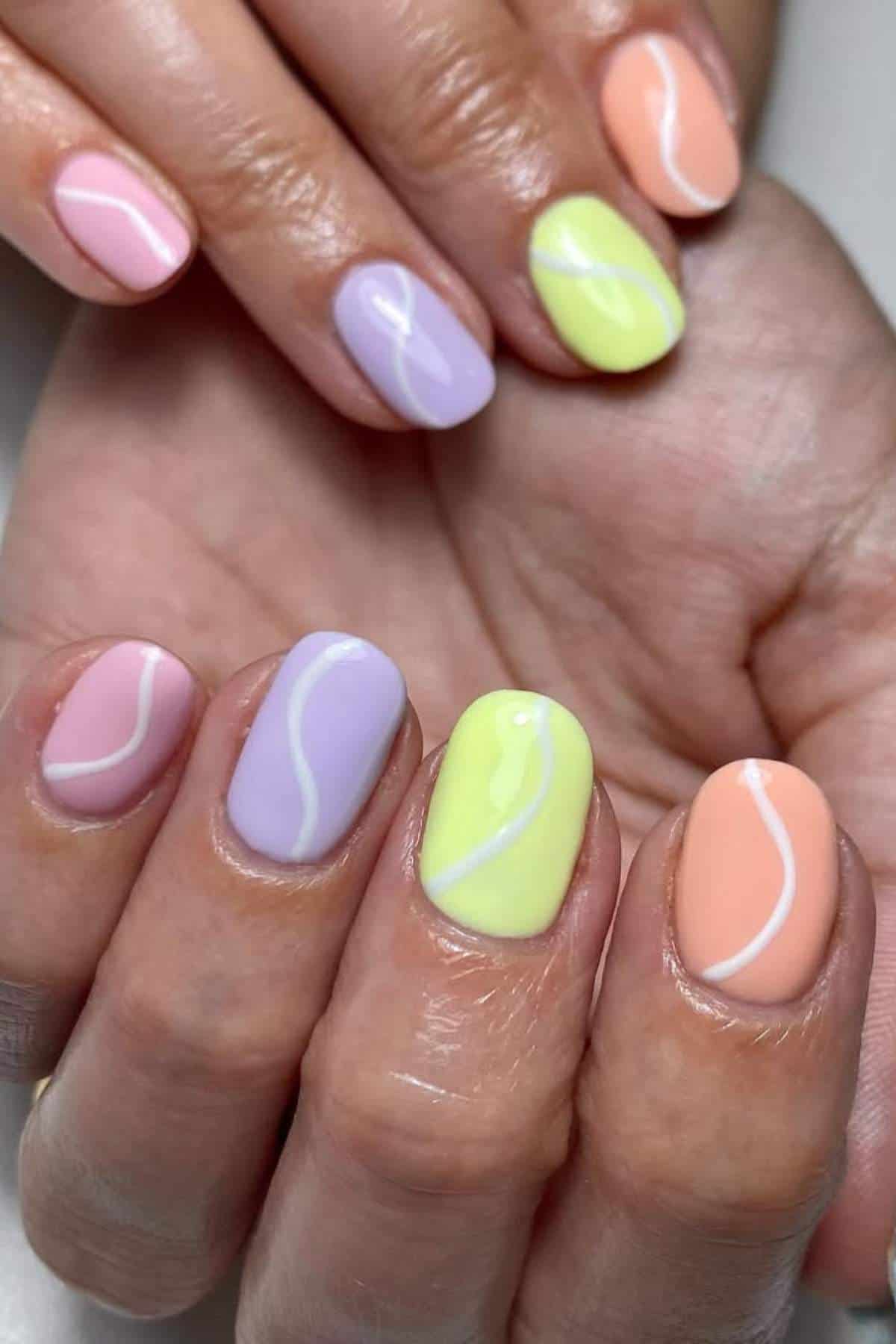 Close-up of hands with pastel-colored nail polish in pink, purple, yellow, and orange, each nail featuring a white wavy line design.